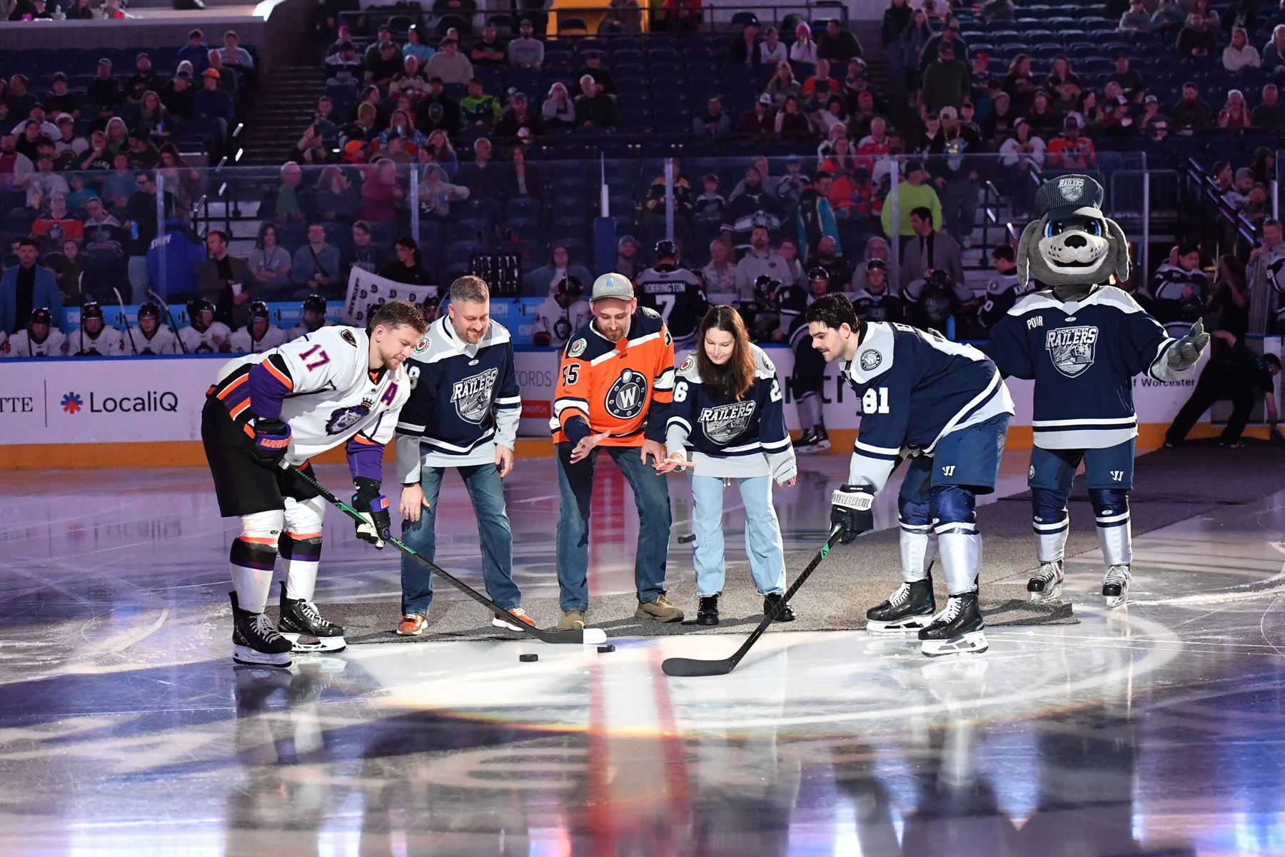 Hockey players and fans on the ice rink during a ceremonial puck drop, with spectators watching from the stands.