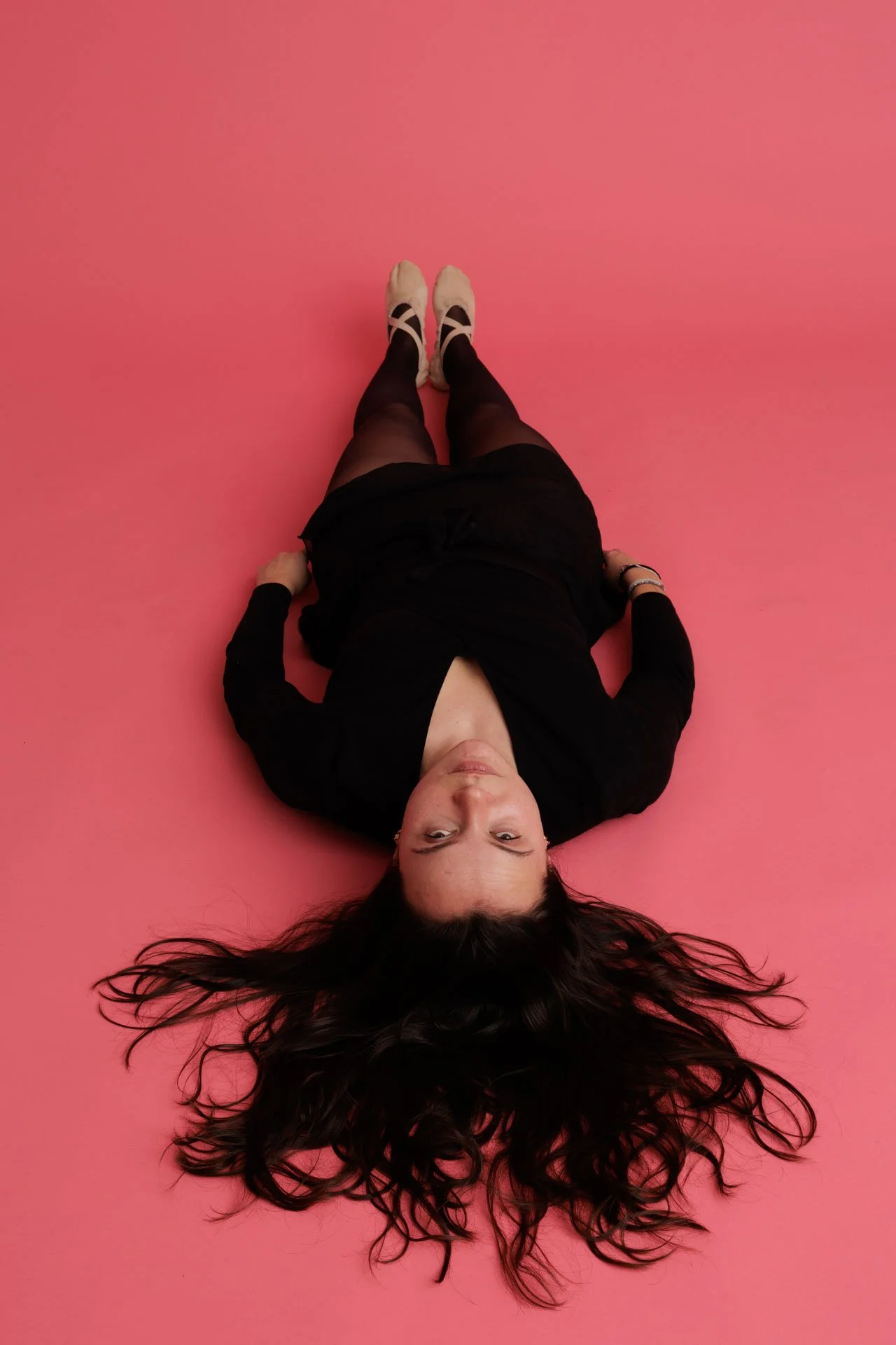 Une femme allongée sur un plan rose, vue de dessus.