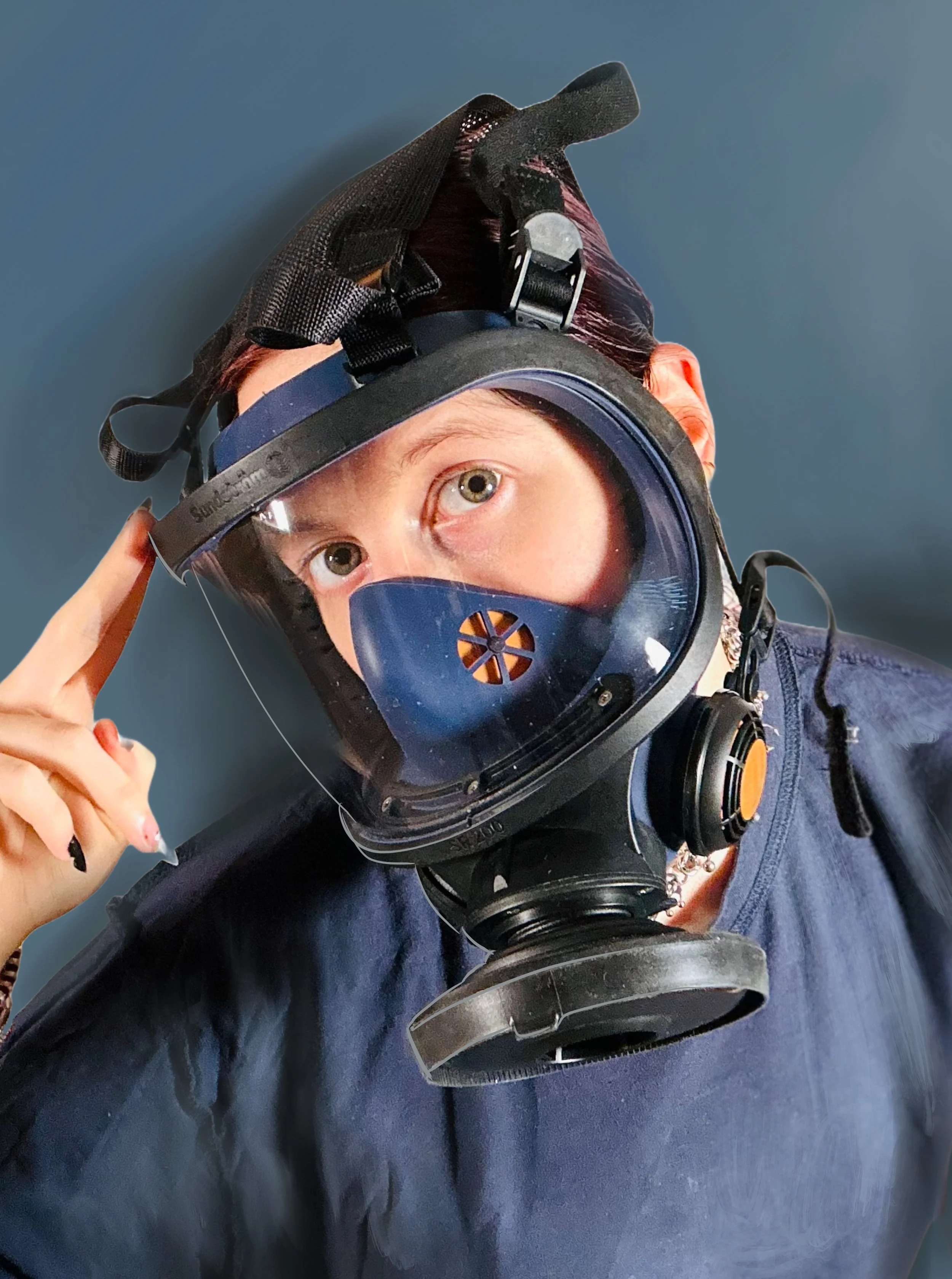 Eine Person trägt eine Atemschutzmaske und eine Schutzbrille, schaut in die Kamera und berührt den Kopf mit der Hand.