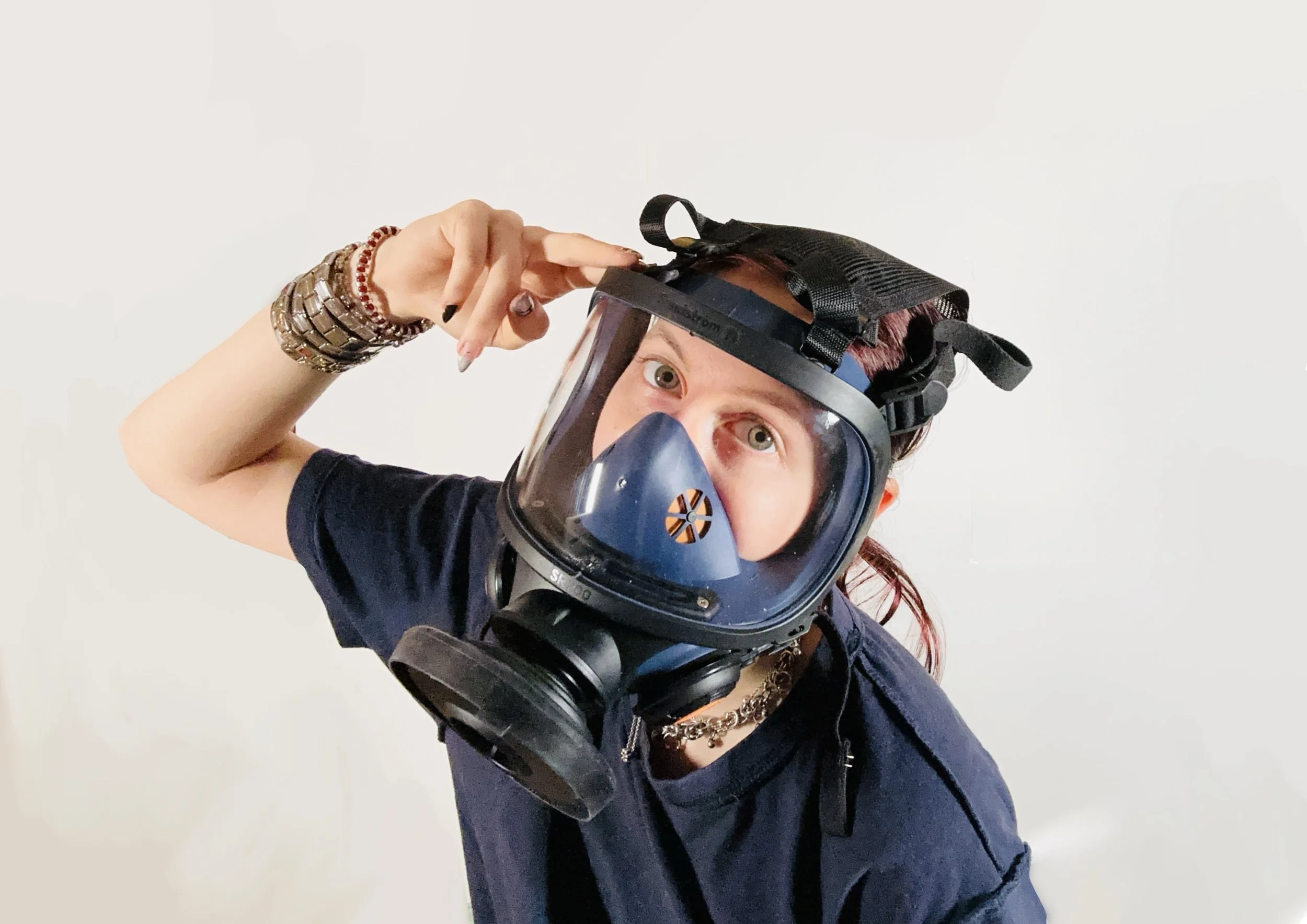 Junge Frau trägt eine Schutzmaske mit Visier und schaut neugierig in die Kamera, während sie an ihrem Kopf eine Schutzmaske anpasst.