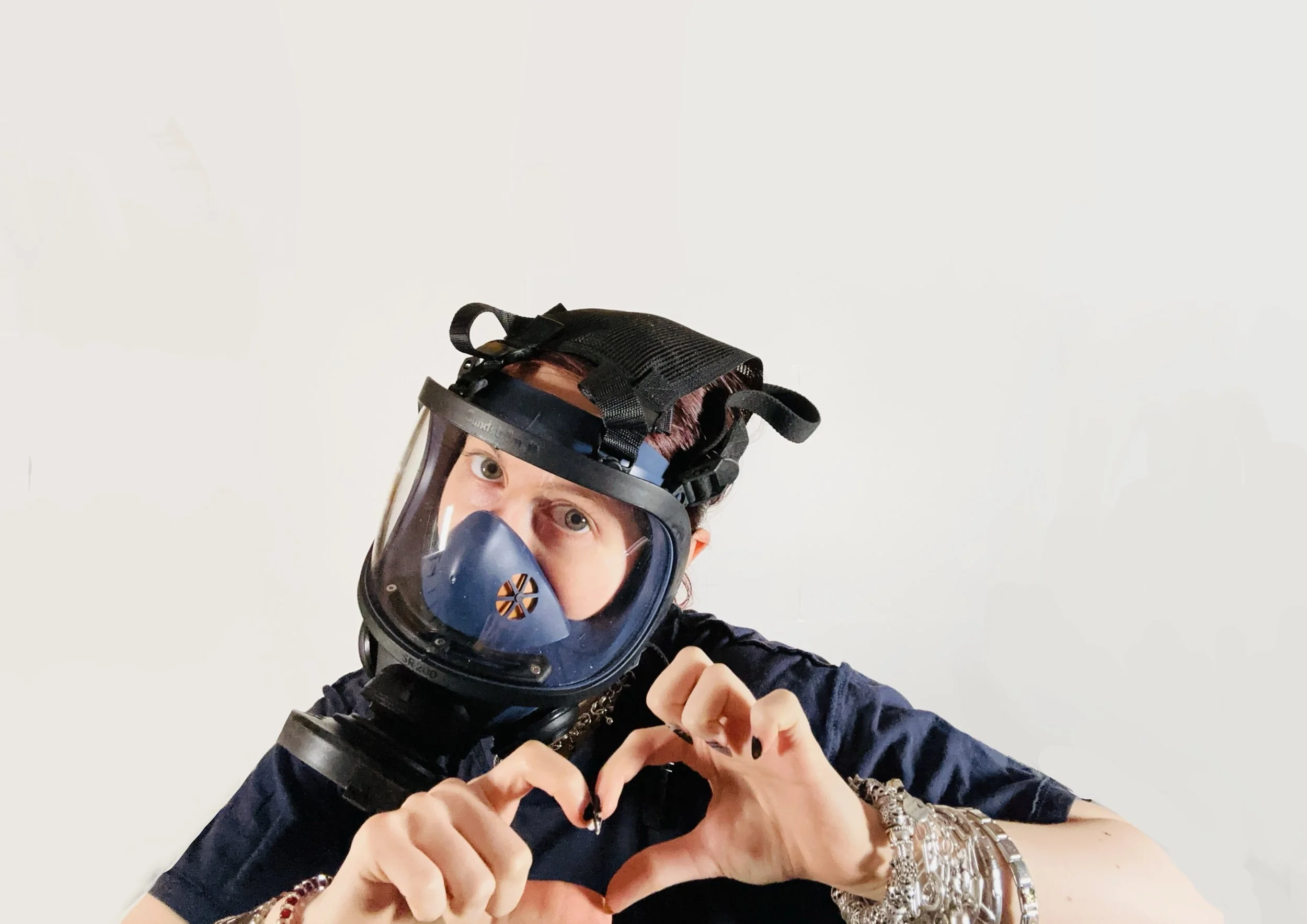 Person trägt einen Schutzhelm mit Atemschutzmaske und bildet Herz mit den Händen.