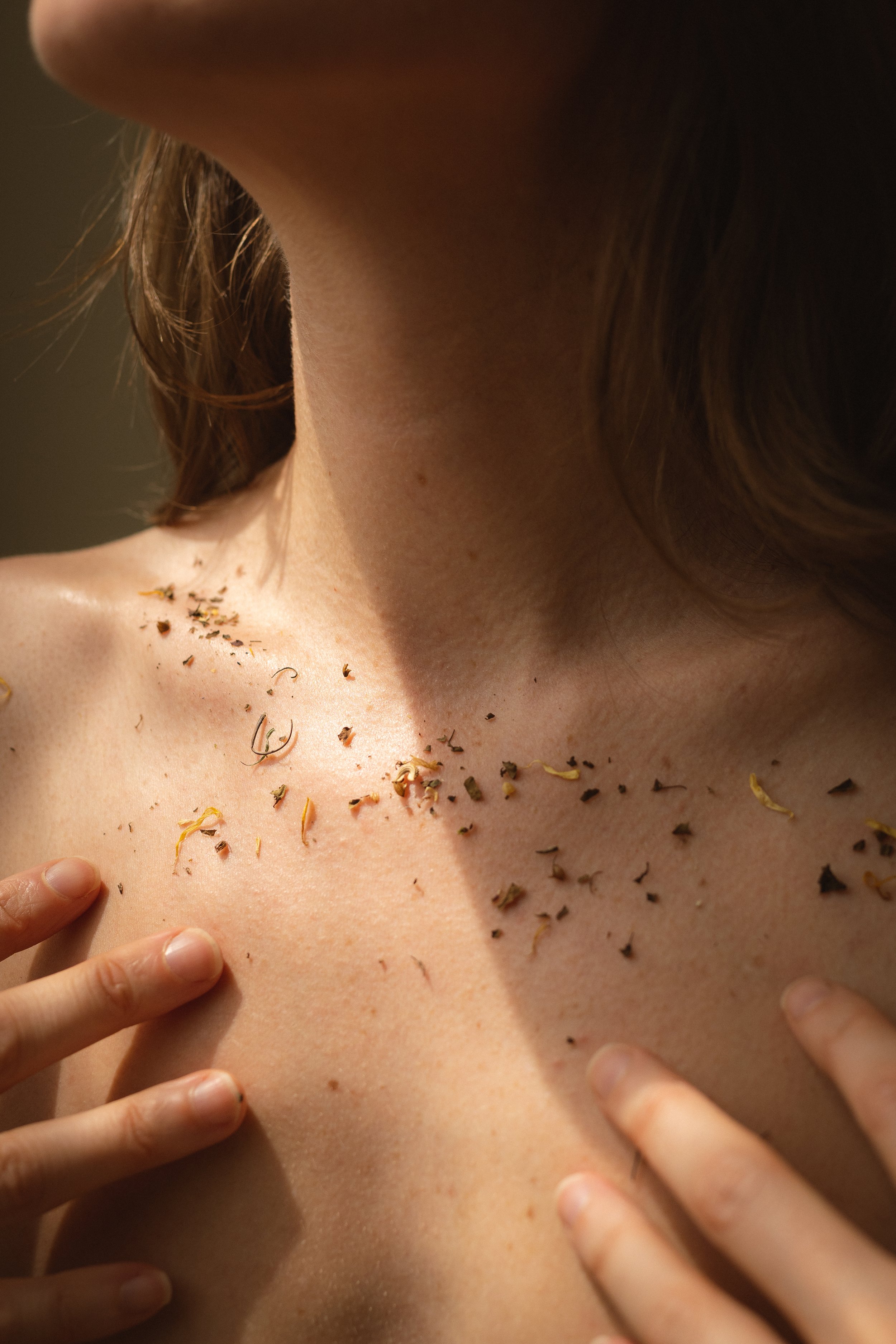 Close-up of a person's neck and shoulders with dried flower petals and small leaves scattered on their skin.