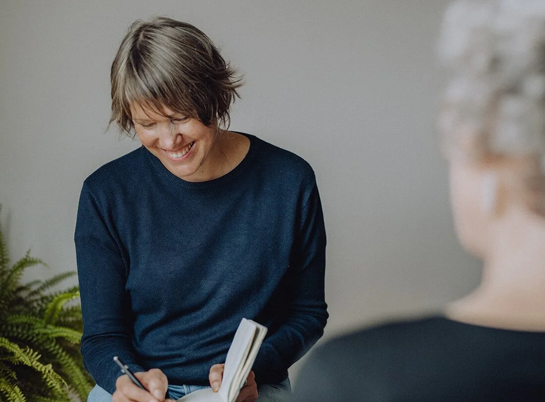 Sara Sommer in Coaching Situation mit Frau sie schreibt in einem Buch und lächelt