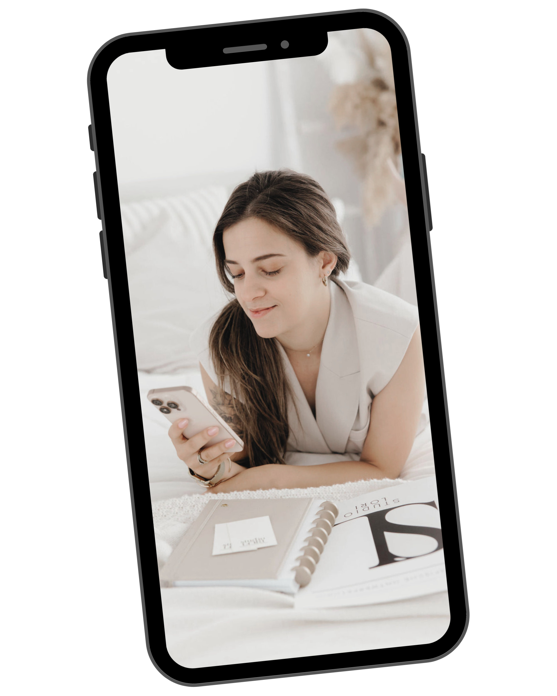 Young woman lying on bed looking at her phone with a planner open in front of her