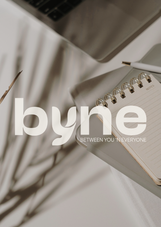 Open notebook with a pen on a desk next to a silver laptop and a plant in a white pot.