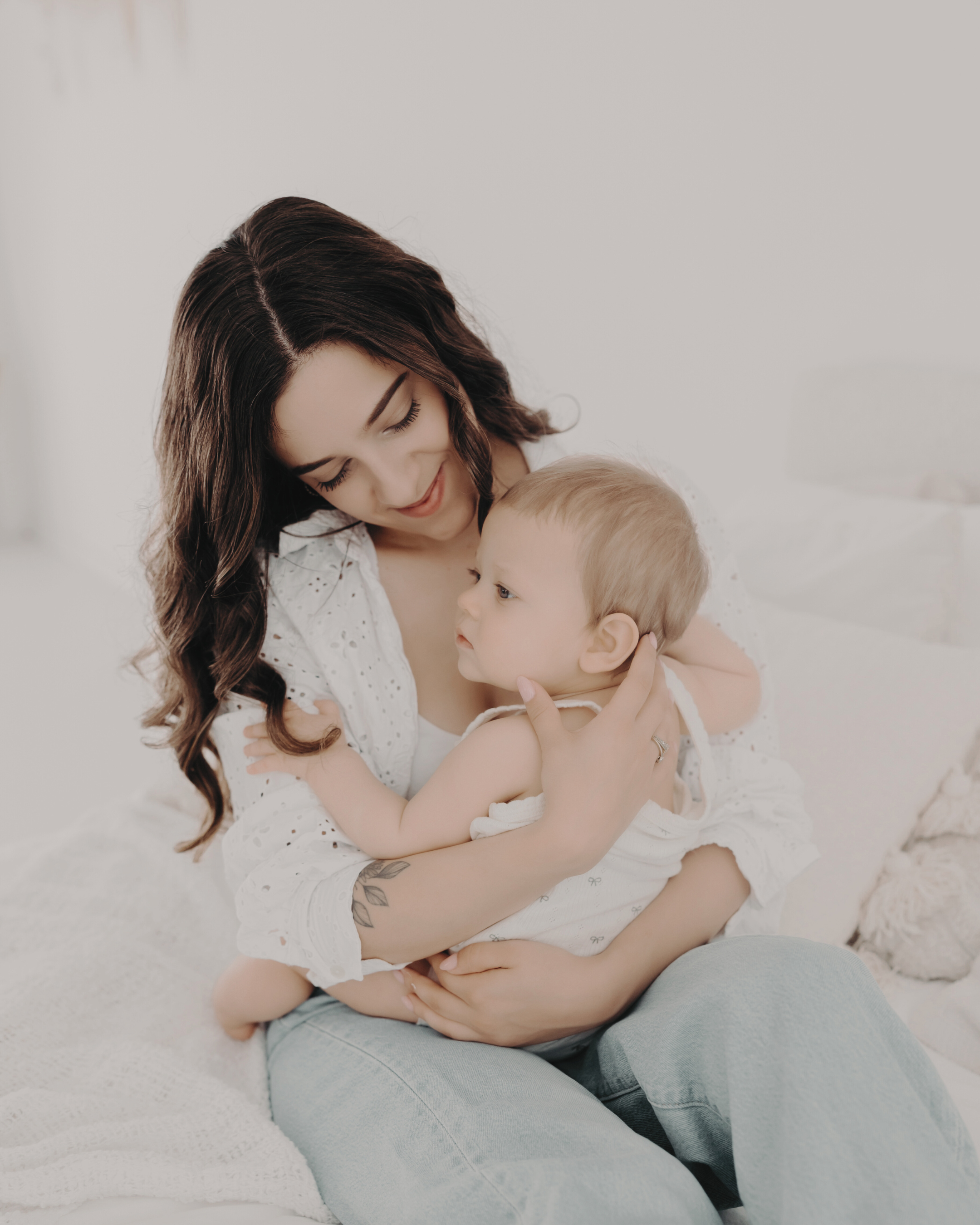 Woman holding a young child in her arms, showing affection in a cozy, white room.