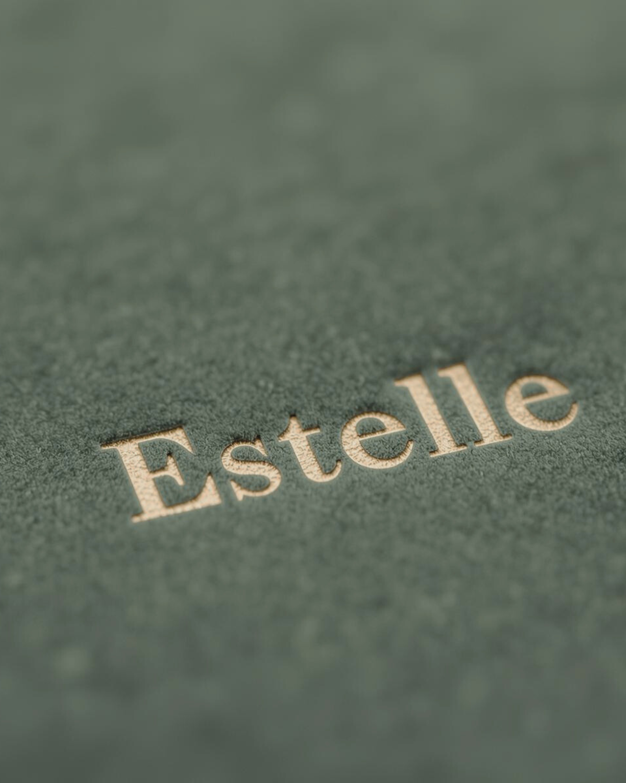 Close-up of the embossed word 'Estelle' on a textured green surface.
