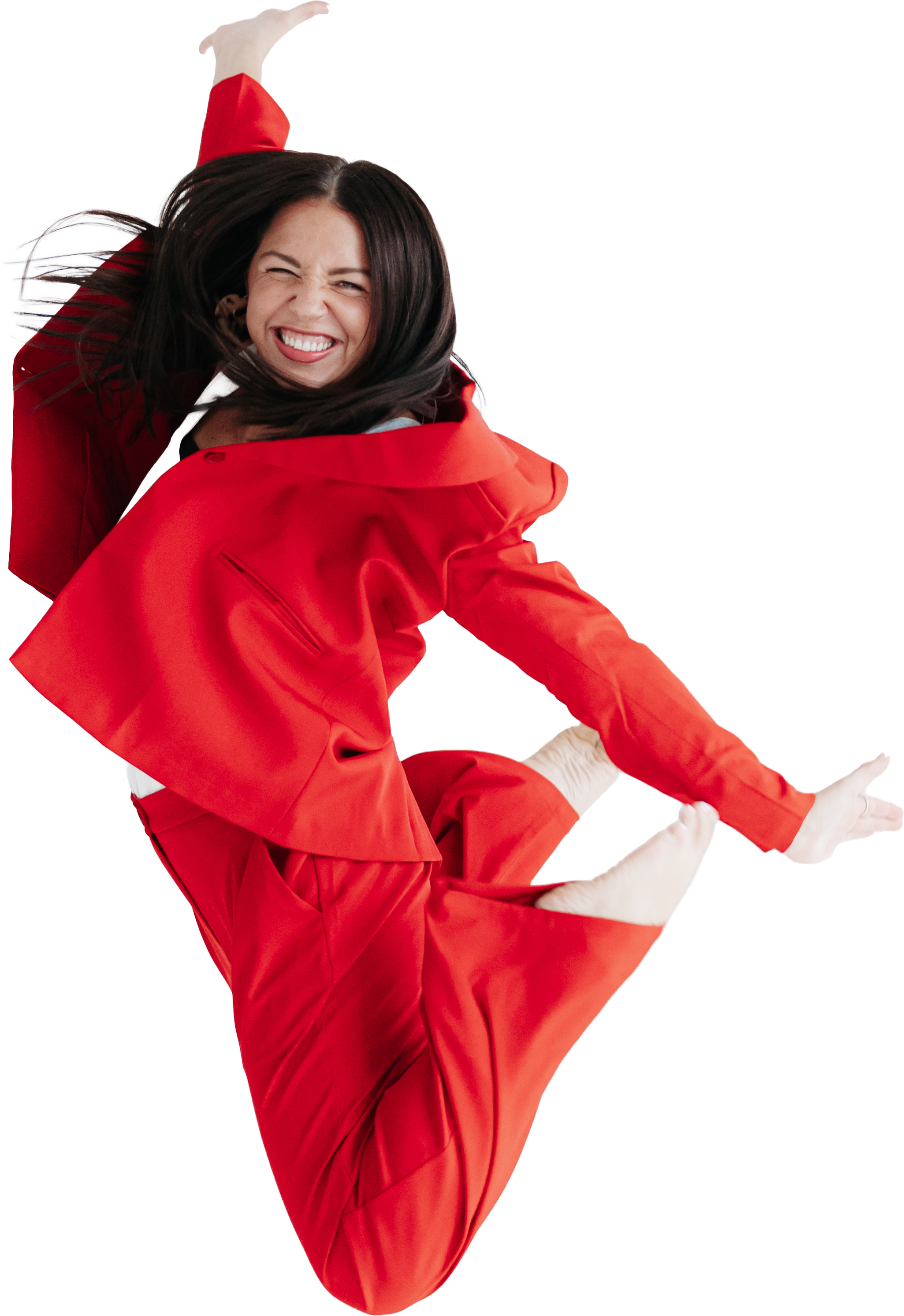 A woman dressed in a red jacket and matching red pants, with long dark hair, smiling and executing a dance leap against a white background.