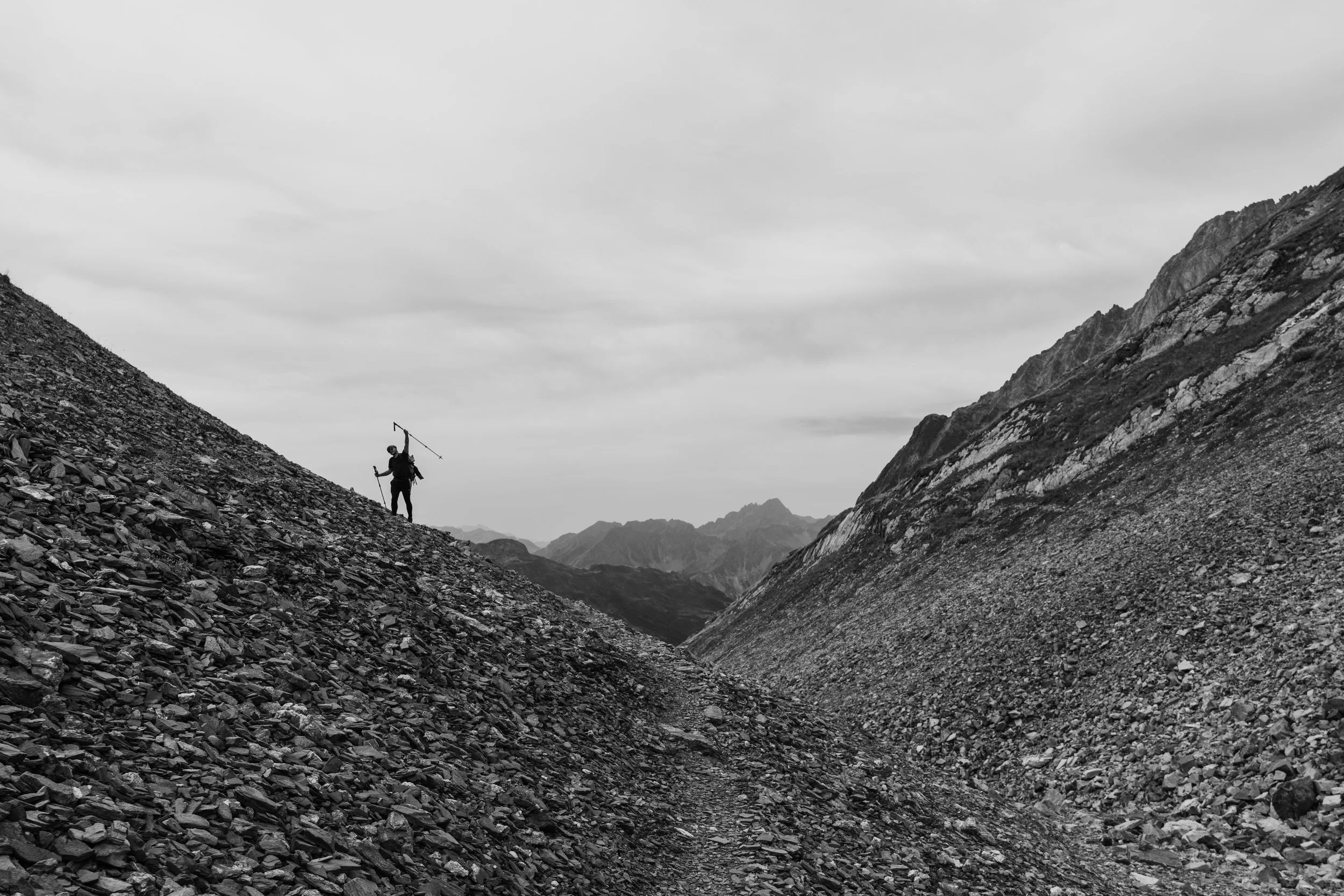 Un randonneur (Karl) avec un équipement de randonnée, se tenant sur une pente rocheuse escarpée dans un paysage montagneux sur le GR TMB.