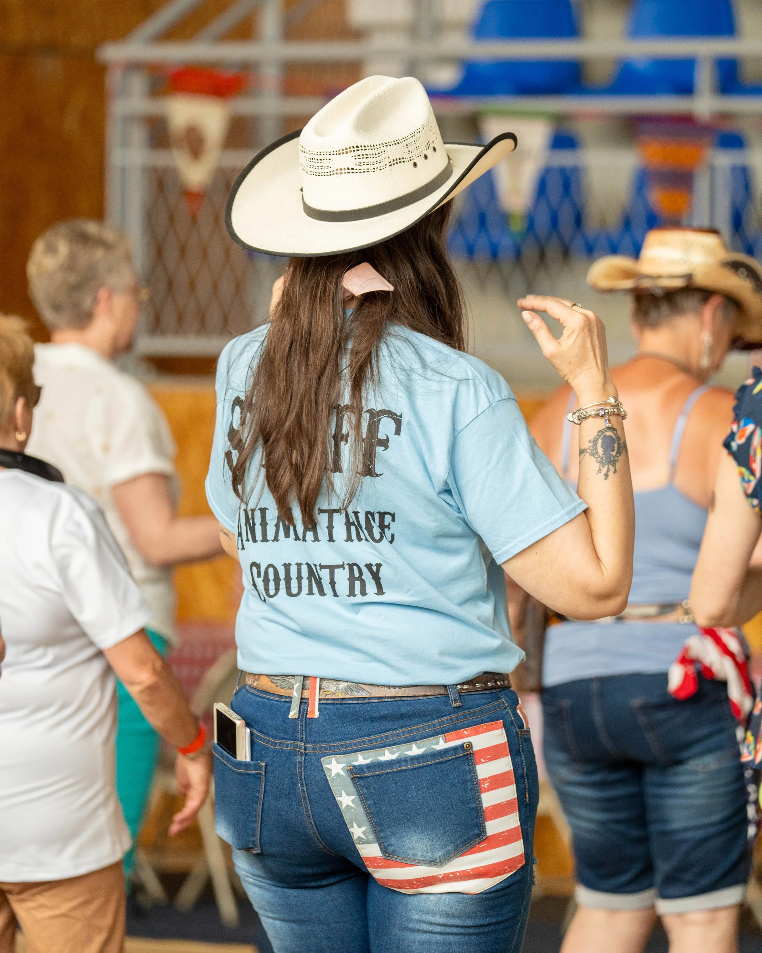 Une femme (Karine) participante à la première édition des "24h pour les voir sourire"portant un chapeau de cowboy blanc et une chemise bleue, en pleine danse country.