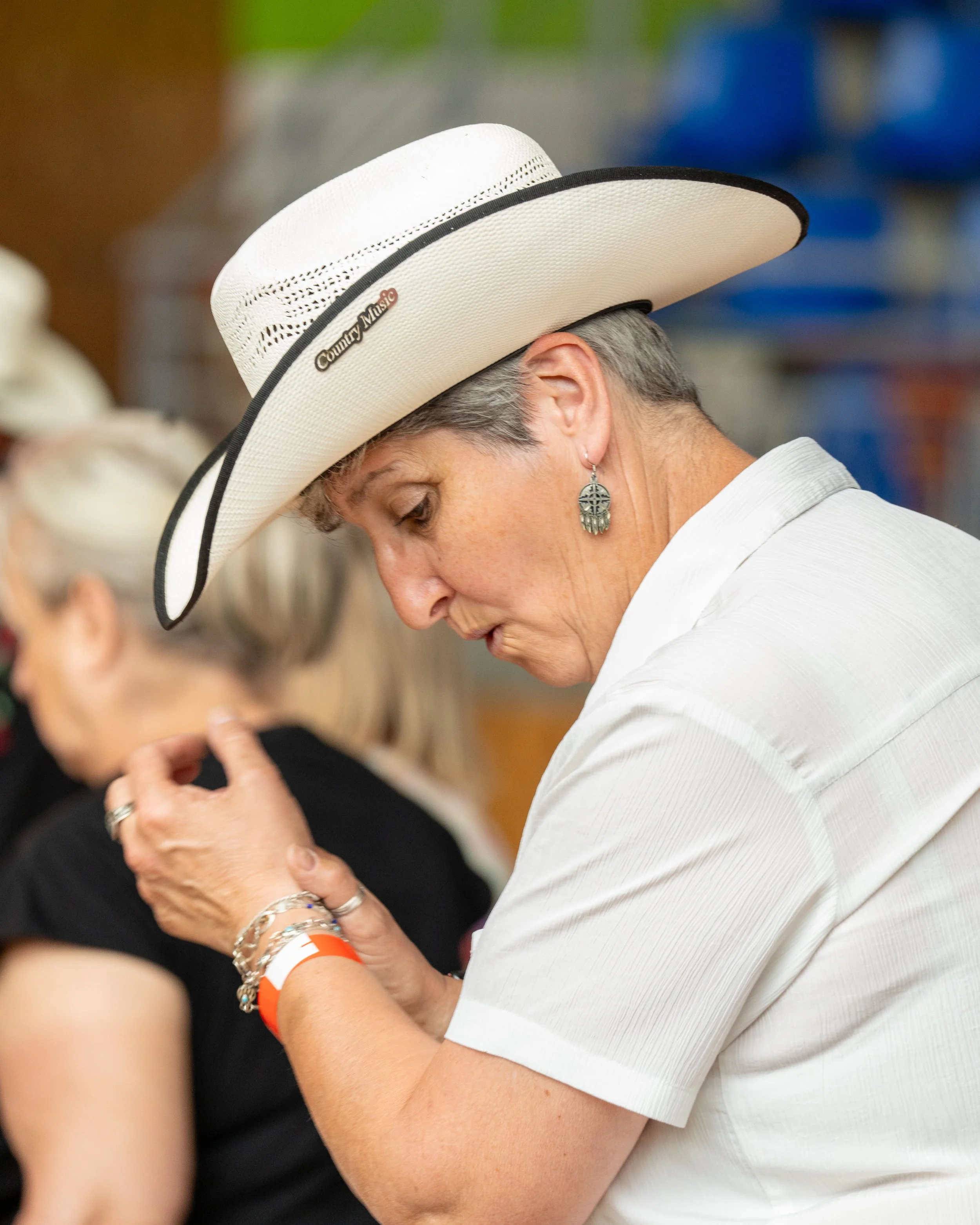 Une femme participante à la première édition des "24h pour les voir sourire" portant un chapeau blanc de cow-boy, une chemise blanche, et des boucles d'oreilles en forme de croix, en pleine danse country.