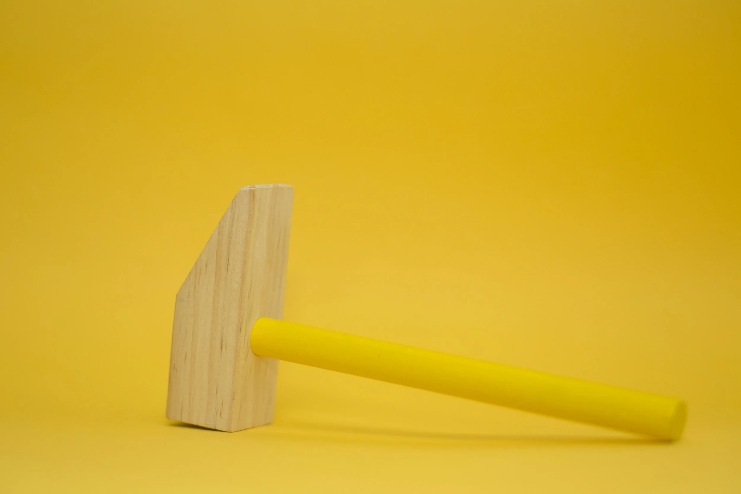 A wooden hammer with a yellow handle lying on a yellow surface against a yellow background.
