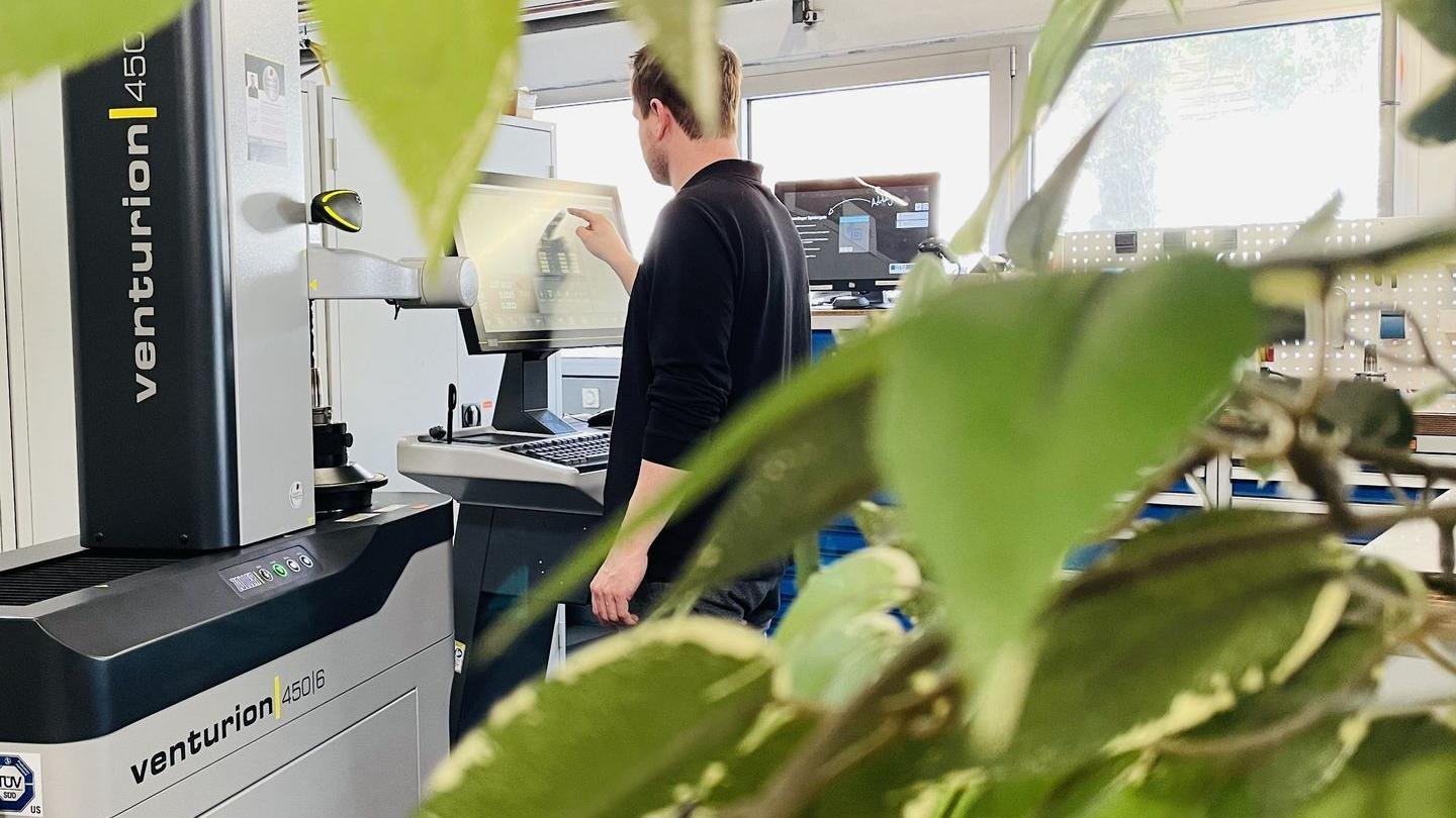 Mann arbeitet an einer Maschine in einem Labor oder Technologielabor, mit grünen Blättern im Vordergrund.