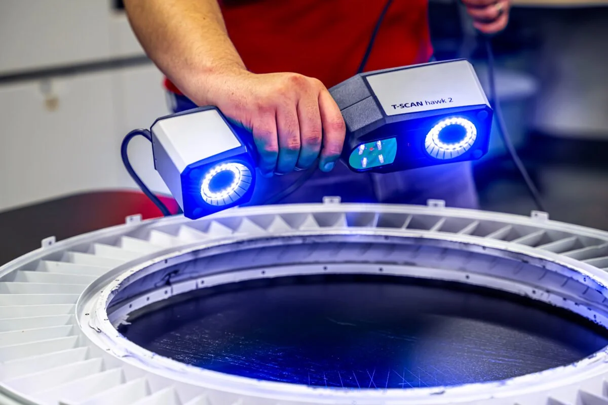 Eine Person hält ein tragbares Lasermikroskop über eine technische Komponente, vermutlich im Rahmen gemessener Analysen oder Wartungen.