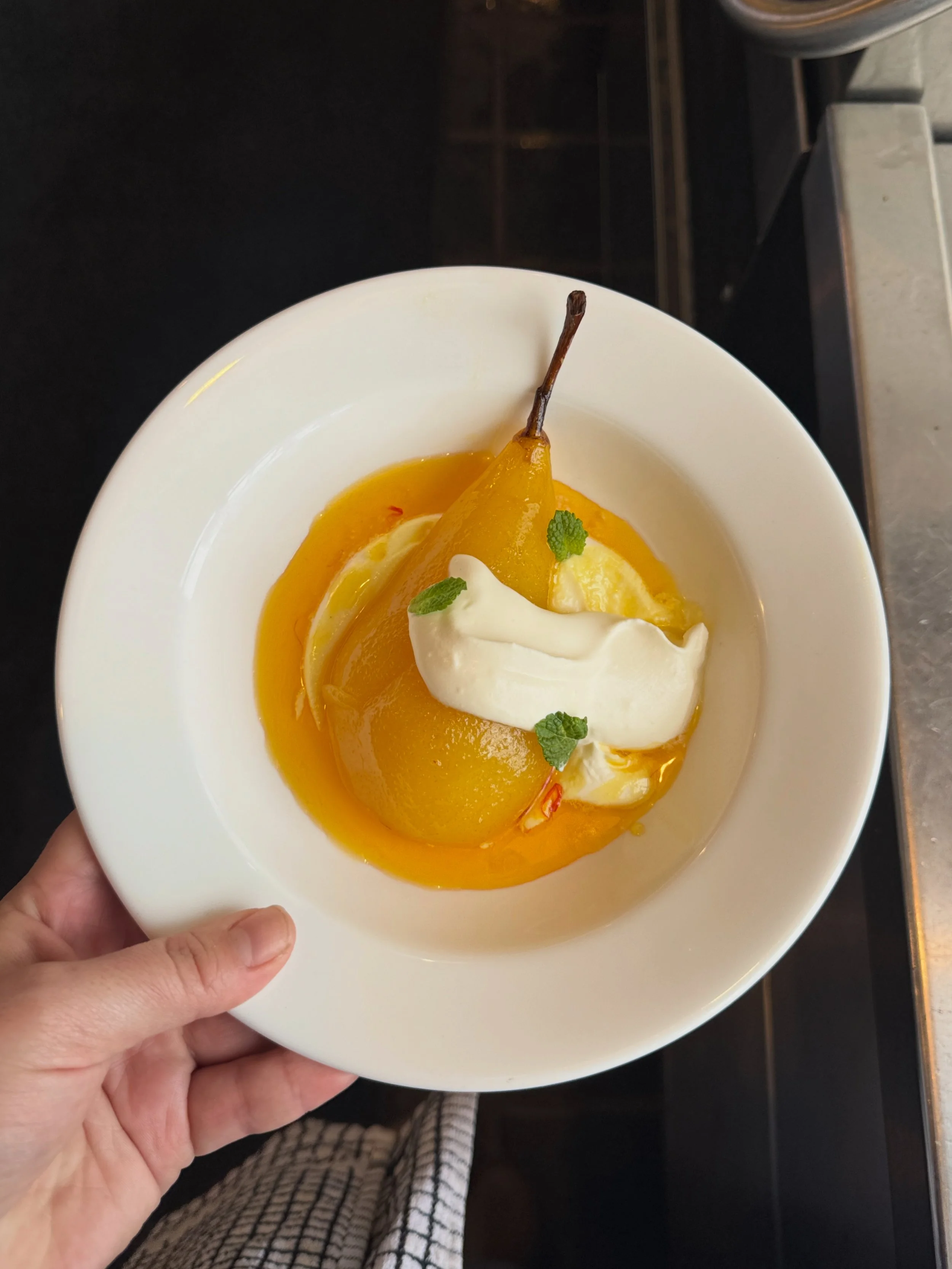 A bowl of poached pear dessert topped with whipped cream and garnished with mint leaves.