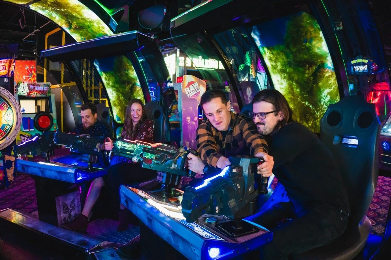 Friends laughing while playing arcade games at Arnold's Family Fun Center