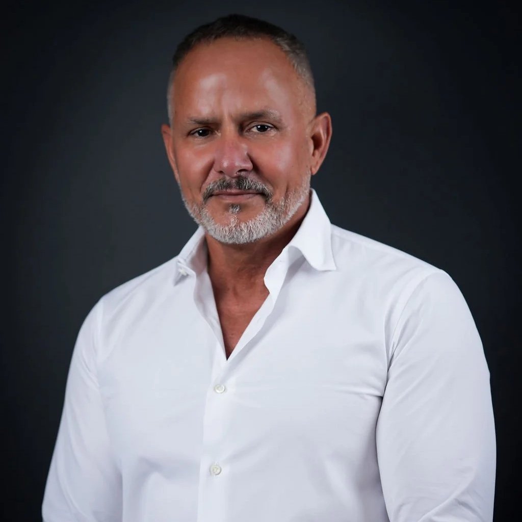 Headshot of a middle-aged man with short hair and a beard, wearing a white button-up shirt, against a dark background.
