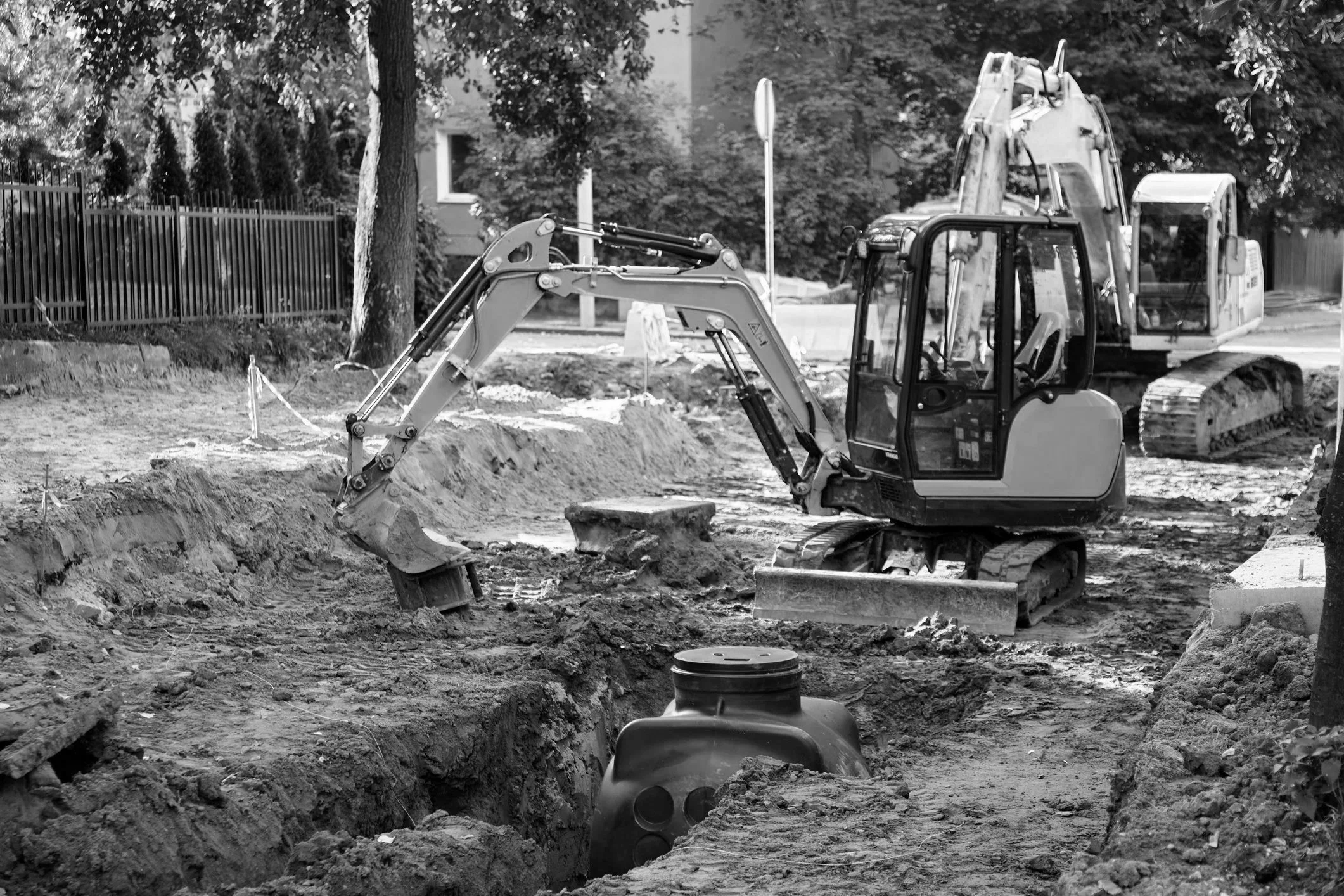 Construction site with excavators and trenches in black and white.