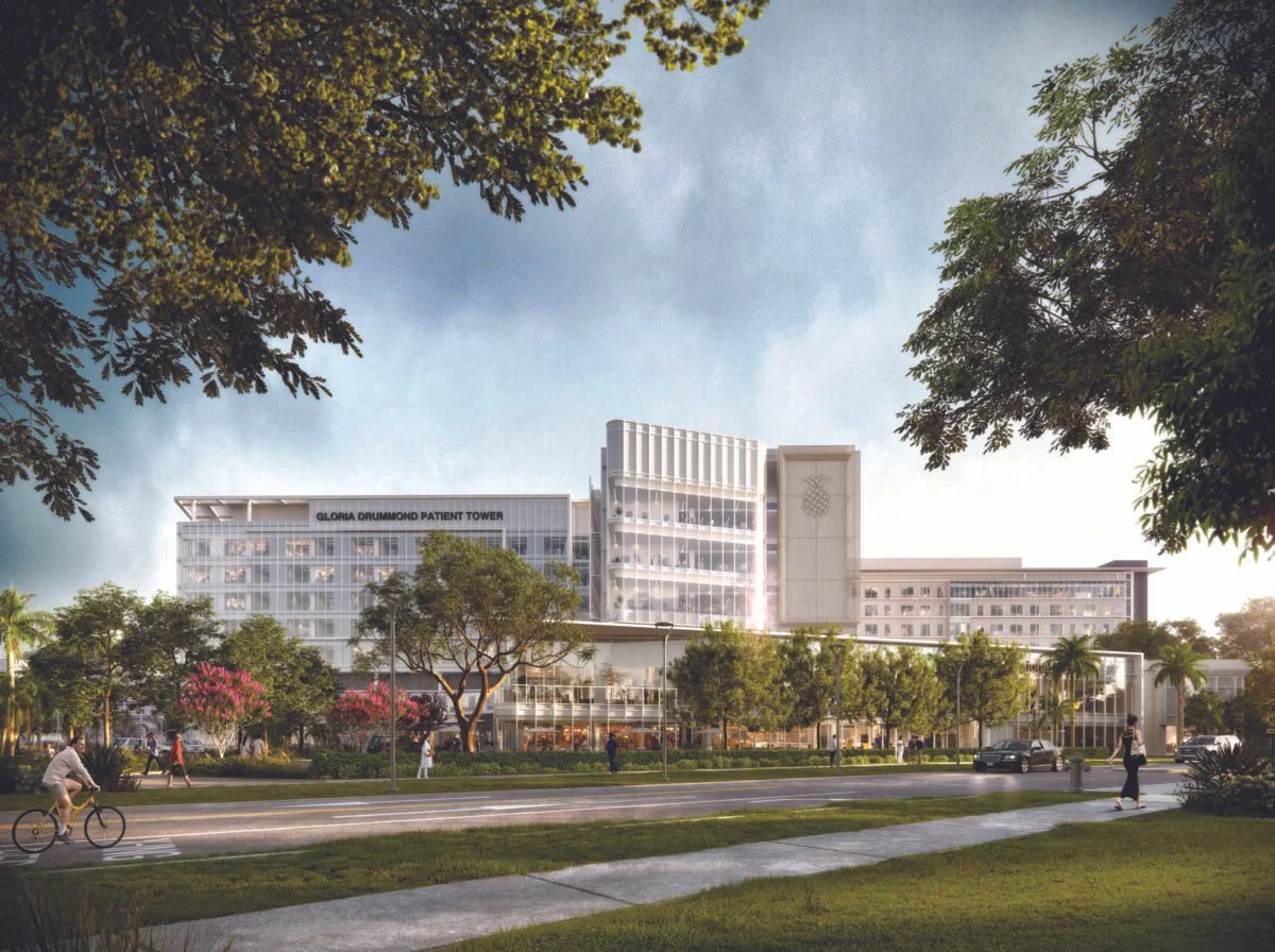 A modern multi-story hospital building labeled "Gloria Drummond Patient Tower," surrounded by trees, people walking, and a person riding a bicycle on a sunny day.