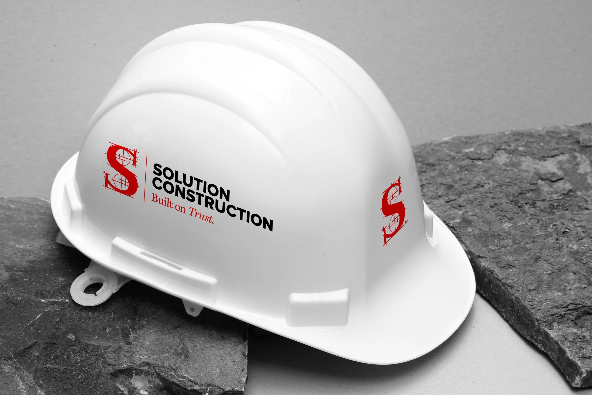 Two white construction helmets with the logo and text "Solution Construction, Built on Trust" placed on a stone surface.