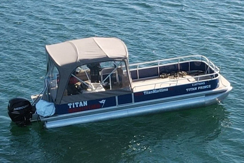 Small motorboat on water with a canopy covering the seating area, labeled 'Titan Marine,' 'Titan Prince,' and 'Titan.'