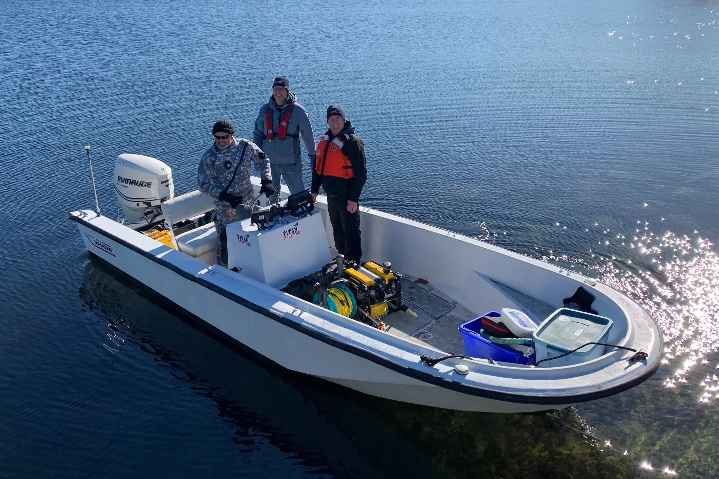 Three men on a white boat with marine equipment on a calm body of water during daytime.