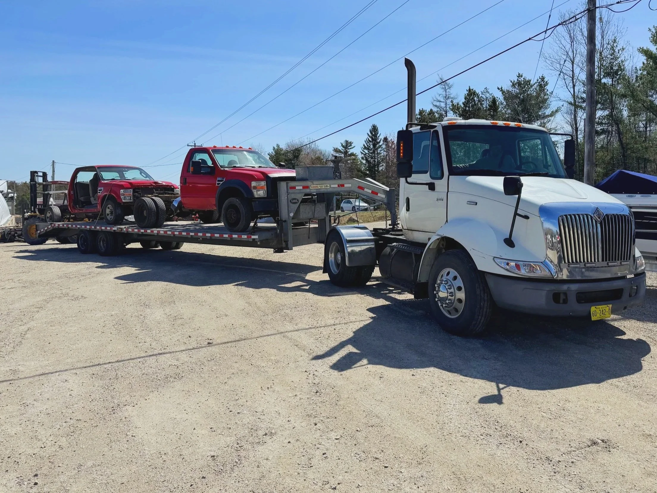White tow truck transporting a partially disassembled red vehicle on a flatbed trailer during daytime.
