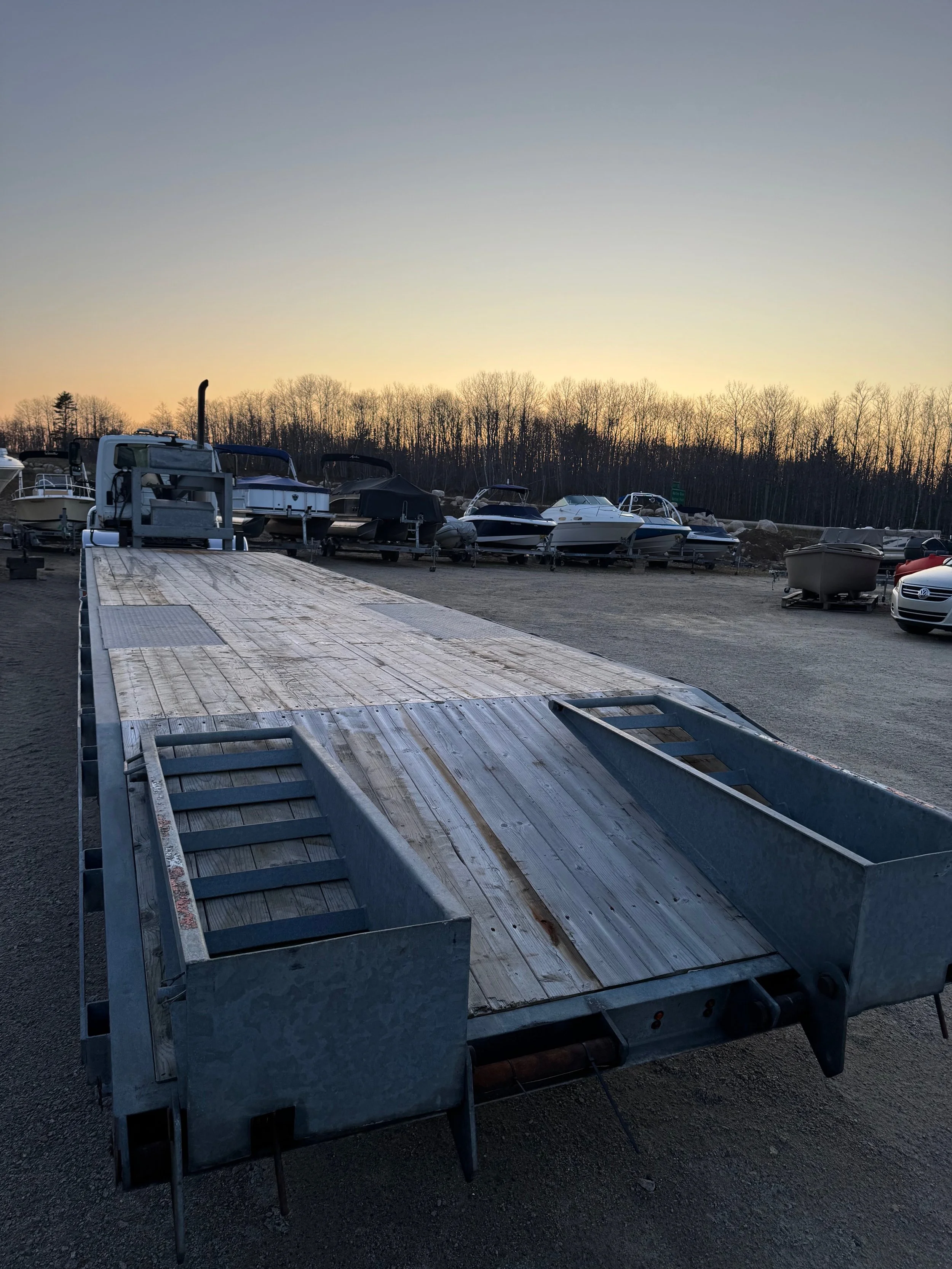 Image of a boat trailer at a marina with boats docked in the background during sunset.