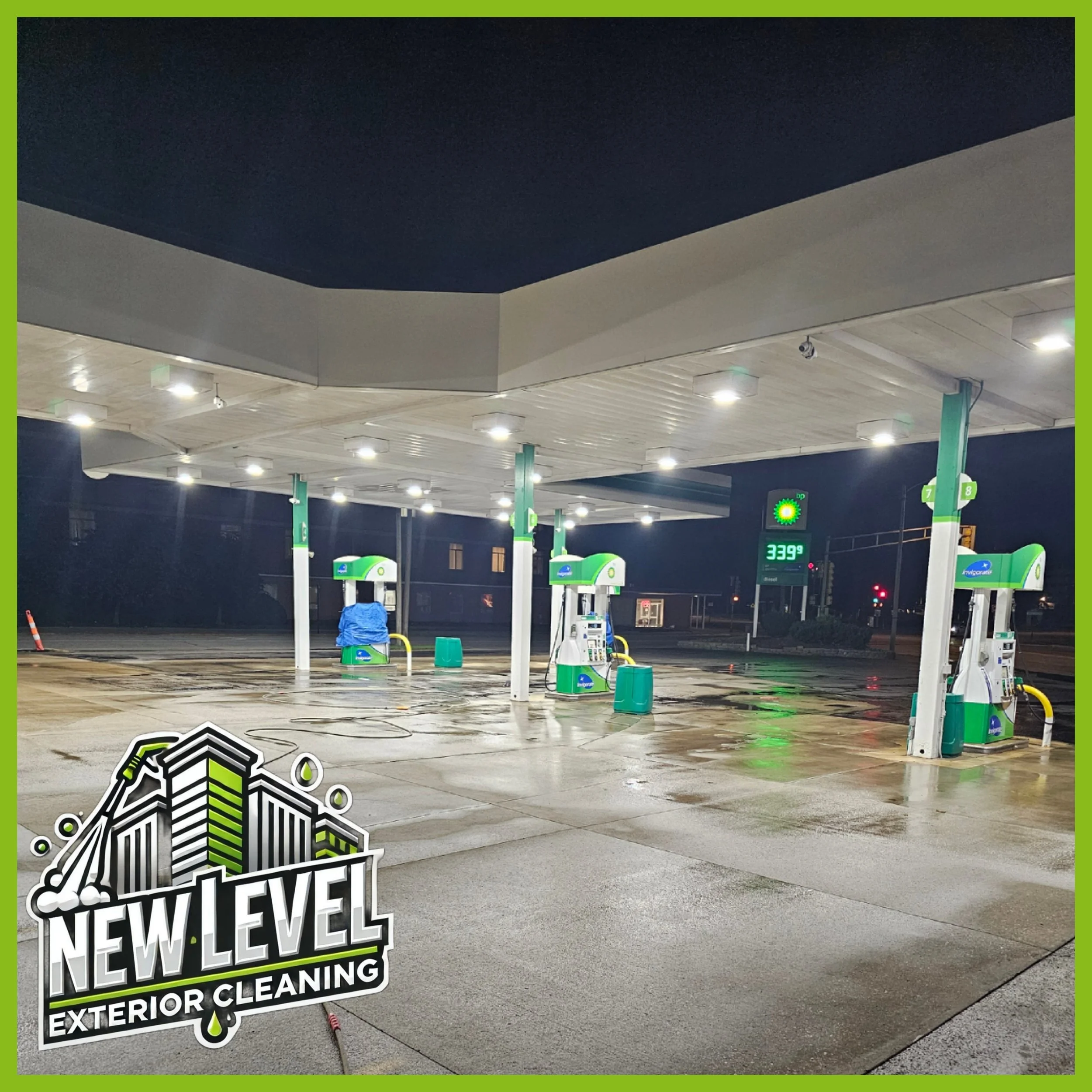 Empty gas station at night with wet pavement, illuminated by overhead lights, and a bright digital sign showing the price per gallon is $3.39, with a logo in the bottom left corner reading "New Level Exterior Cleaning."
