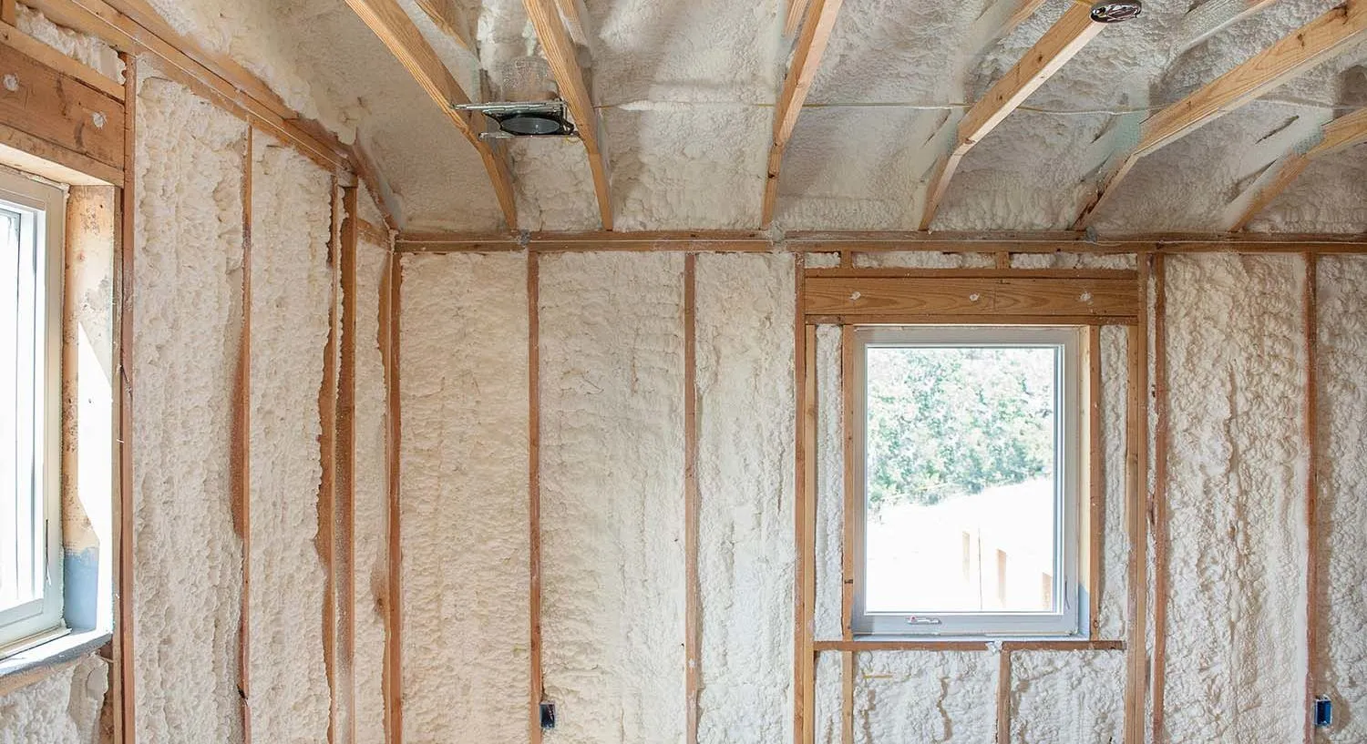Interior of a room under construction with insulation installed, uncovered wooden framing, and two windows.