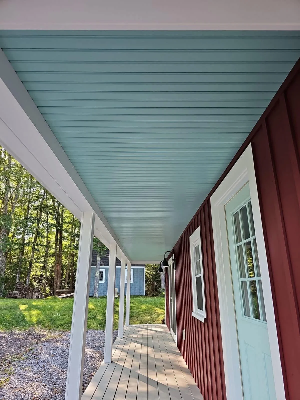 Front porch of a house with a red exterior and white-trimmed windows, oak trees in the background, and a light blue ceiling on the porch ceiling.