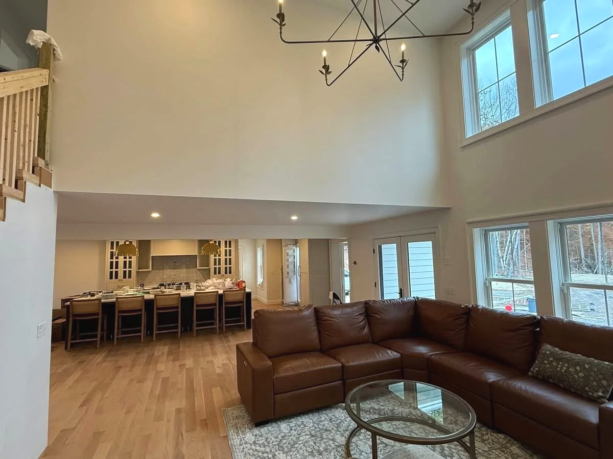 Open-concept living room with leather sectional, round glass coffee table, hardwood floors, large windows, and a chandelier