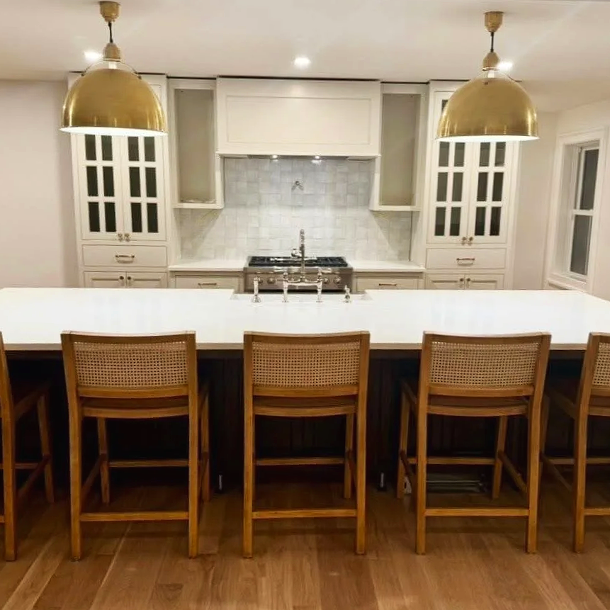 Modern kitchen with white cabinets, a marble backsplash, a stove, and a large white island with wooden bar stools. Two gold pendant lights hang over the island.