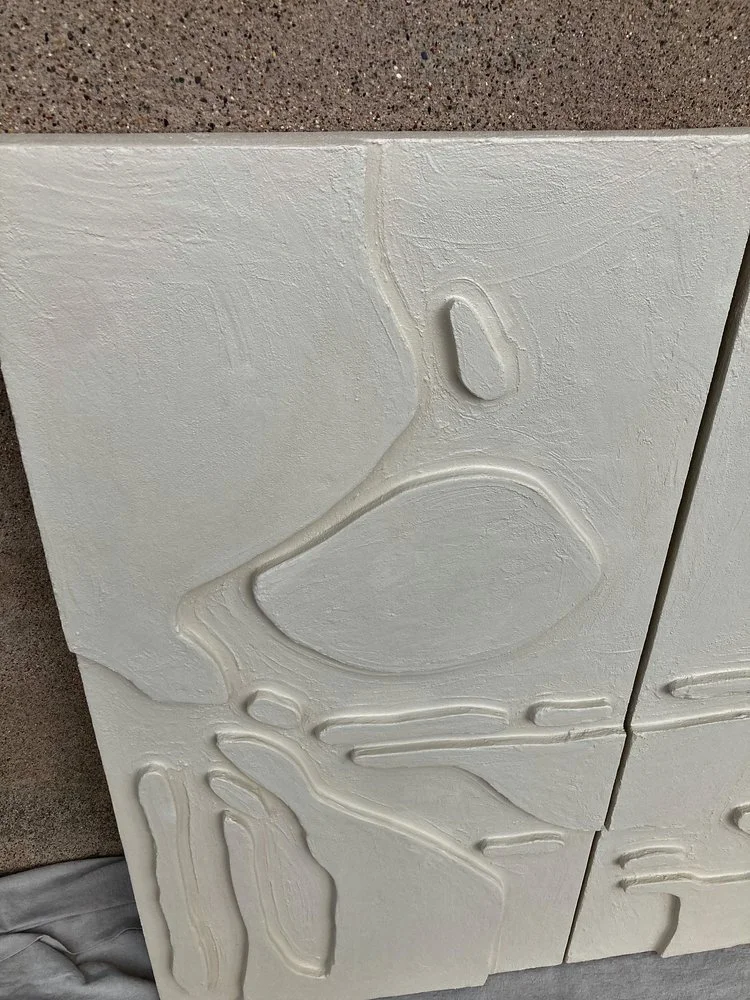 Close-up of a textured white wall with abstract carved patterns, next to a concrete surface.