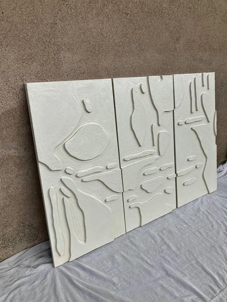 Abstract textured white artwork on four large vertical panels with organic, flowing lines, leaning against a beige wall, on a white cloth-covered surface.