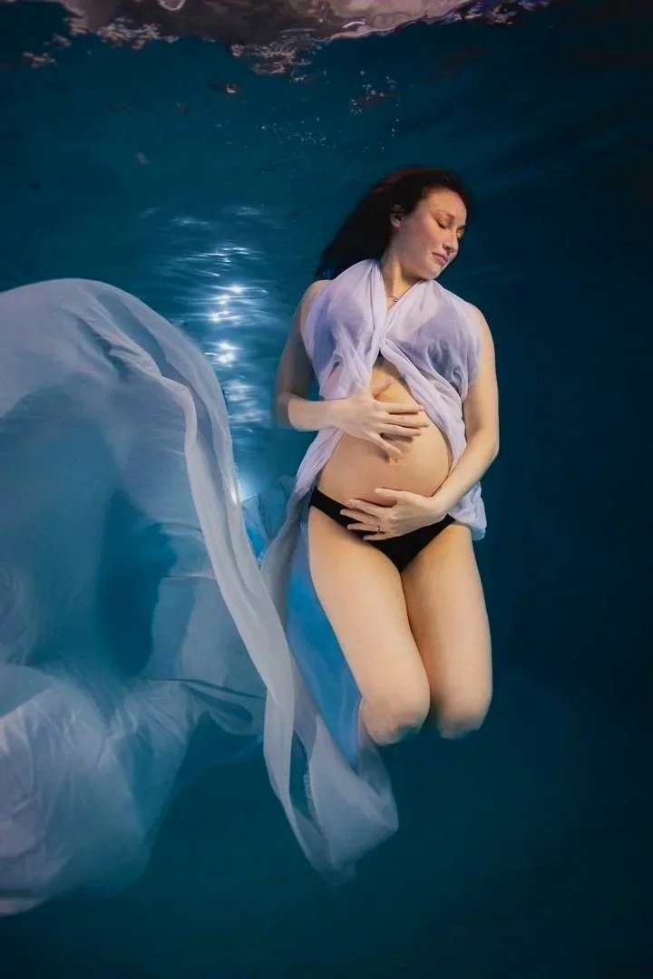 Underwater maternity portrait of young pregnant woman in flowy gown with serene, peaceful expression