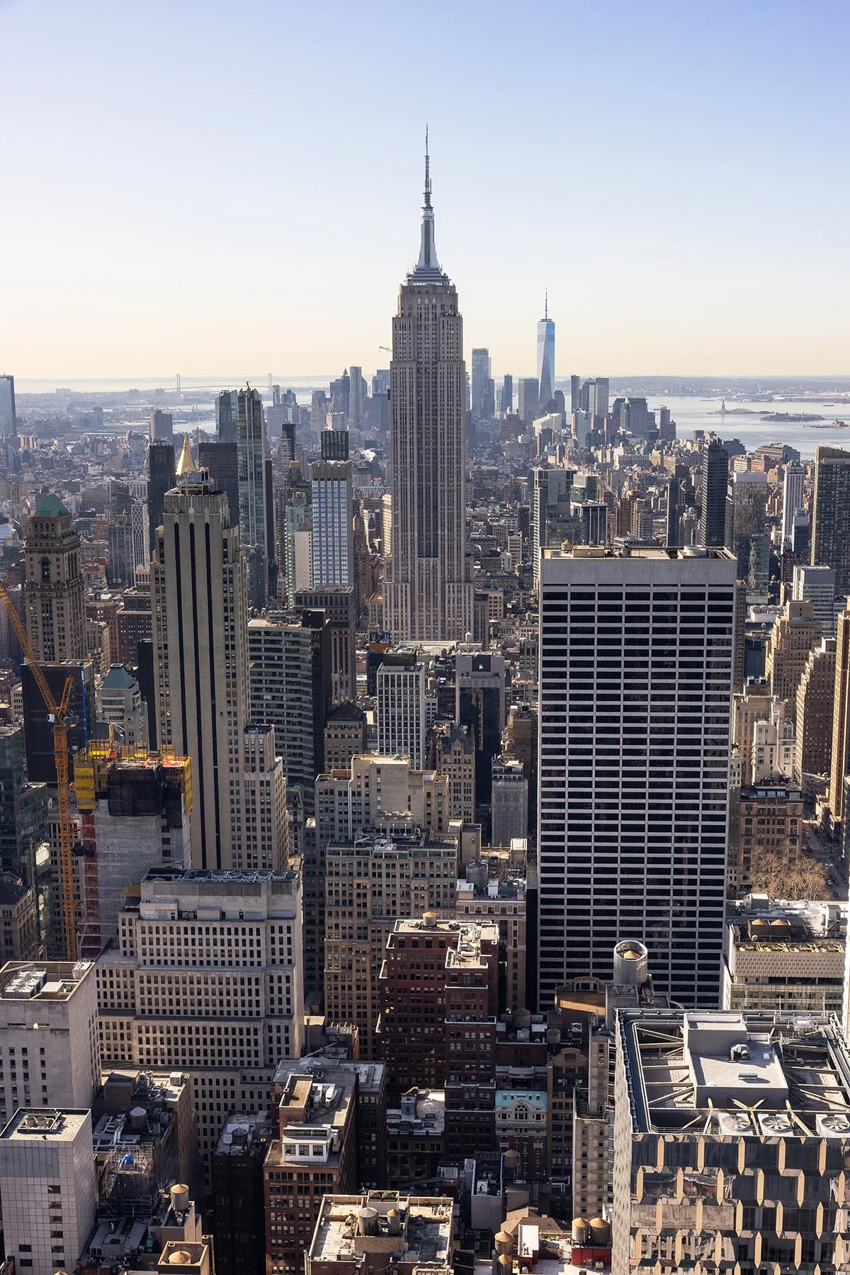 Skyline view of Manhattan with the Empire State Building and One World Trade Center in the background, during daytime with clear sky.