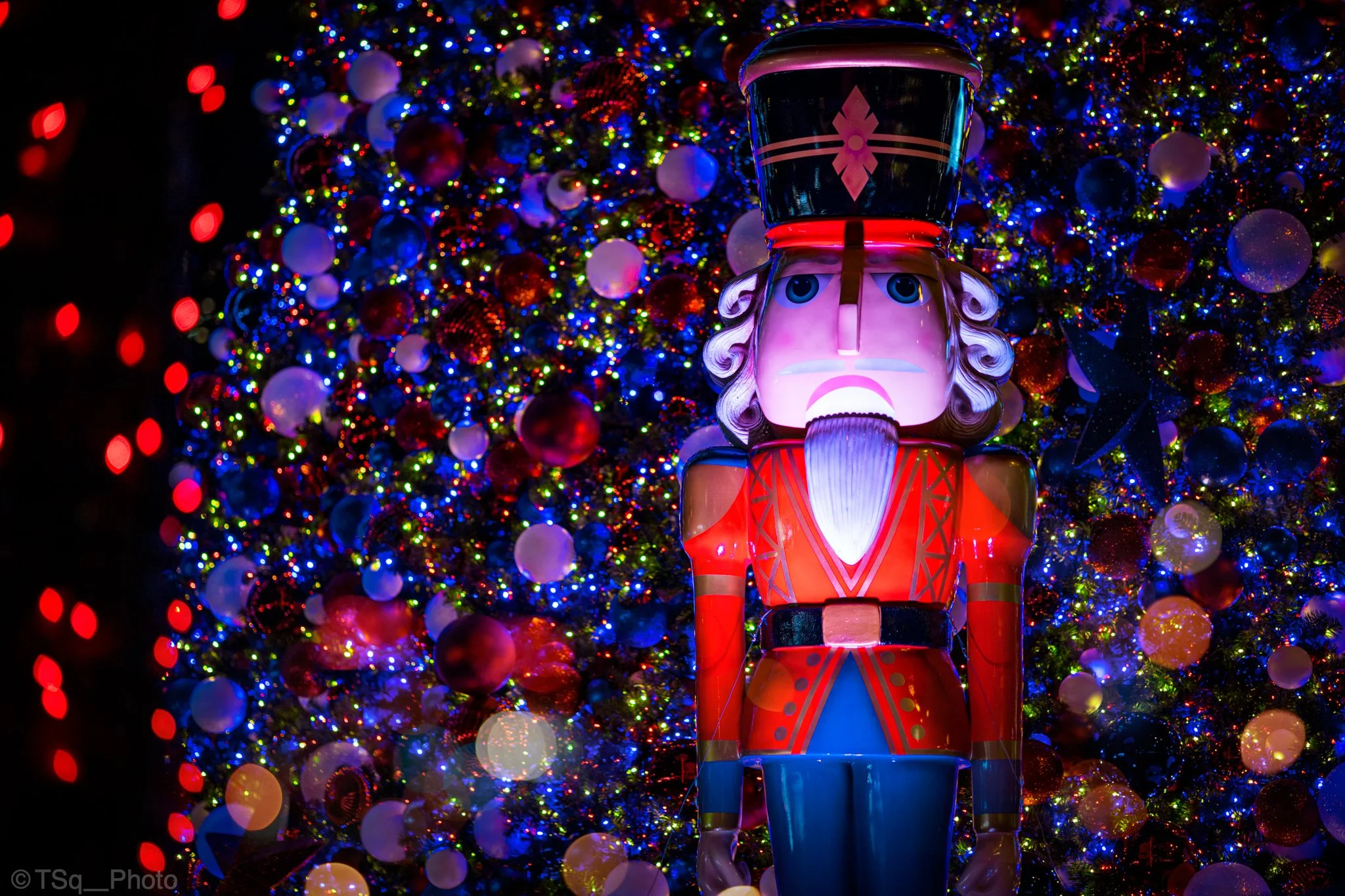 Colorful Christmas scene with a nutcracker decoration in front of a decorated Christmas tree with multicolored lights and ornaments.