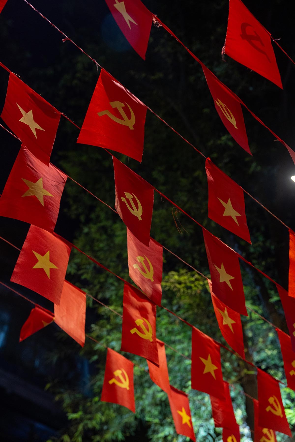 Red flags with yellow stars and yellow hammer and sickle symbols, hanging on strings at night. The flags are associated with communist and socialist countries.