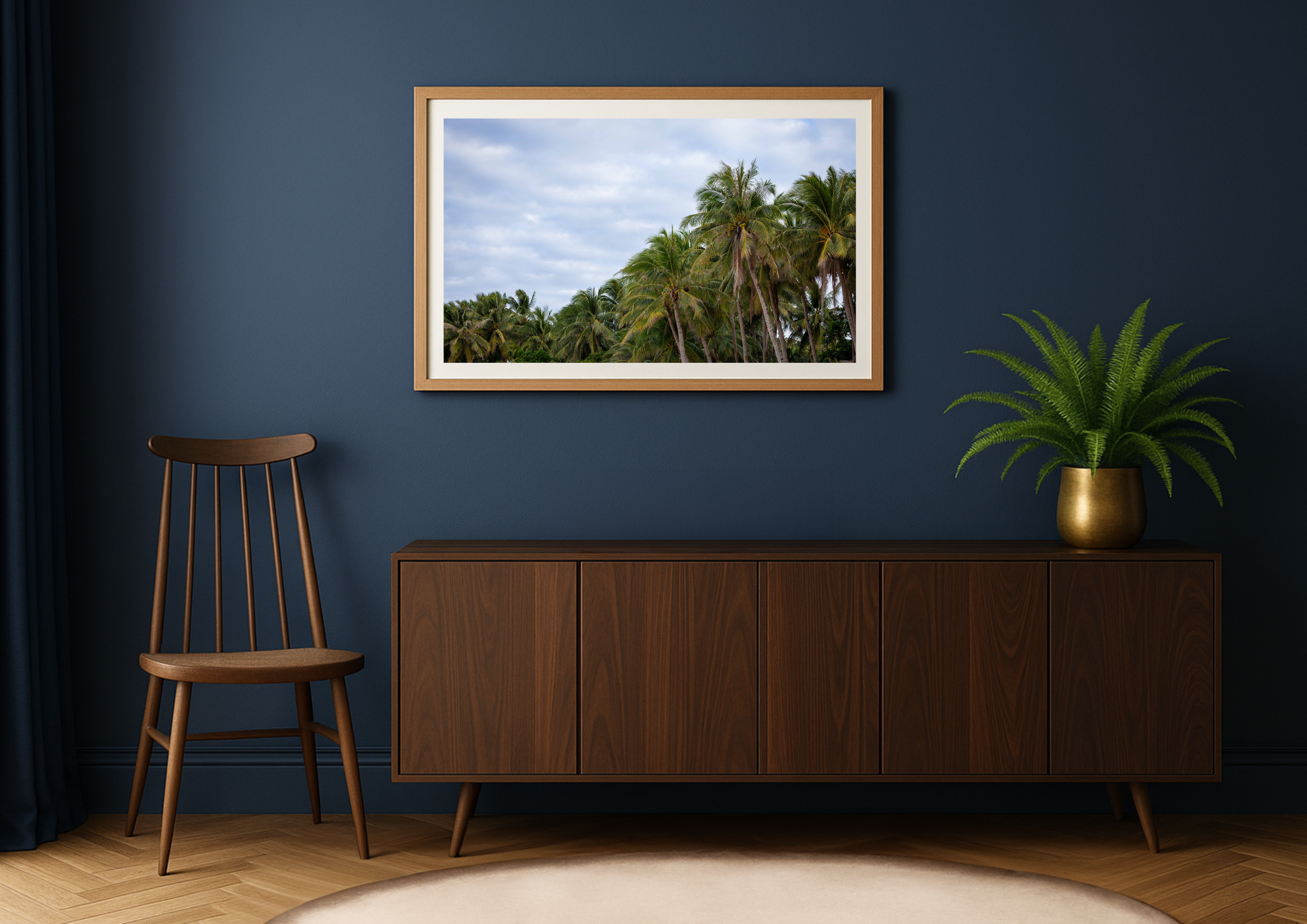 Interior of a room with a framed picture of palm trees on the wall, a wooden sideboard, a wooden chair, and a potted fern on the sideboard.