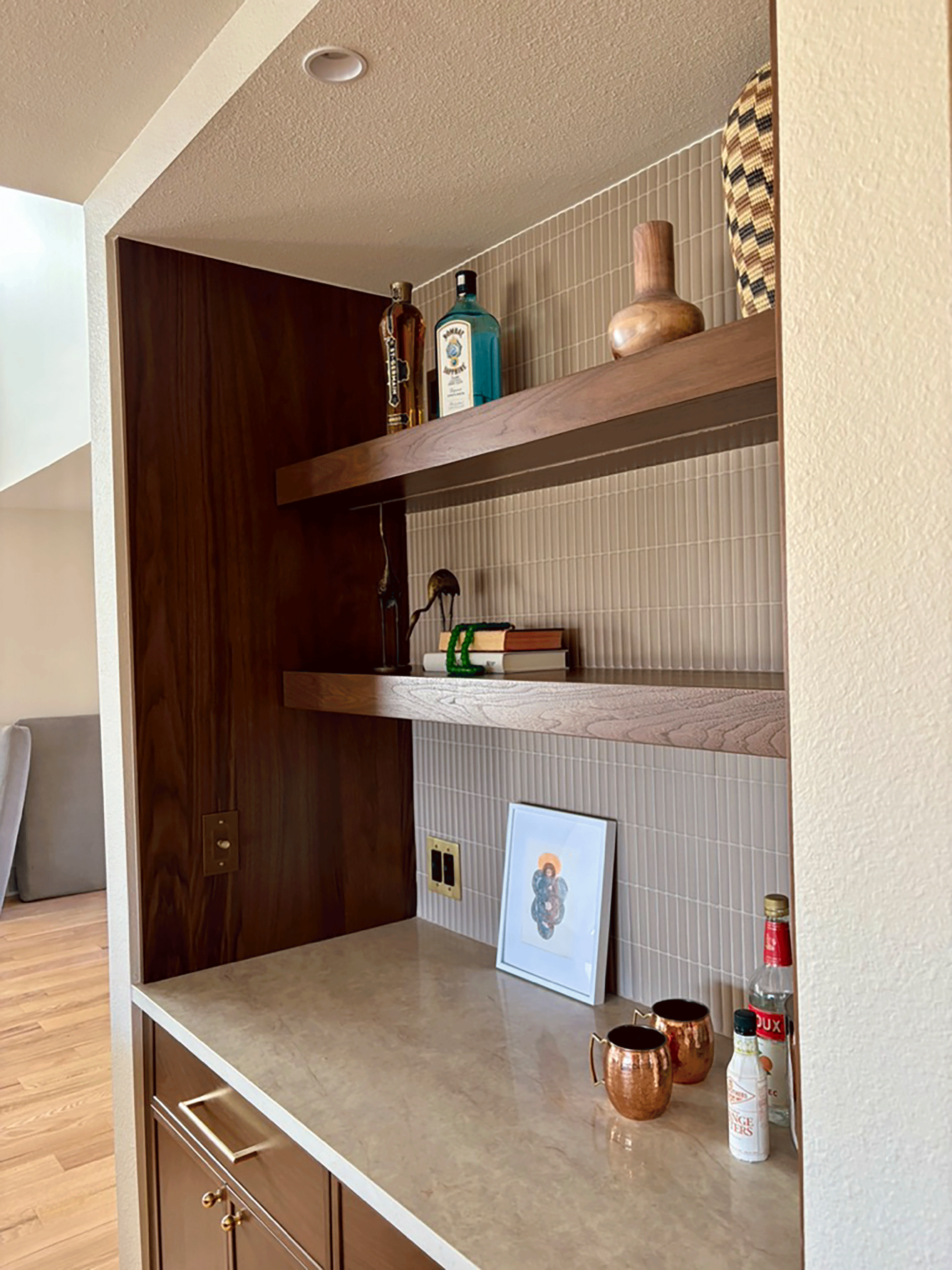 A kitchen countertop with decorative copper cups, a framed artwork, and bottles of alcohol against a tiled wall.