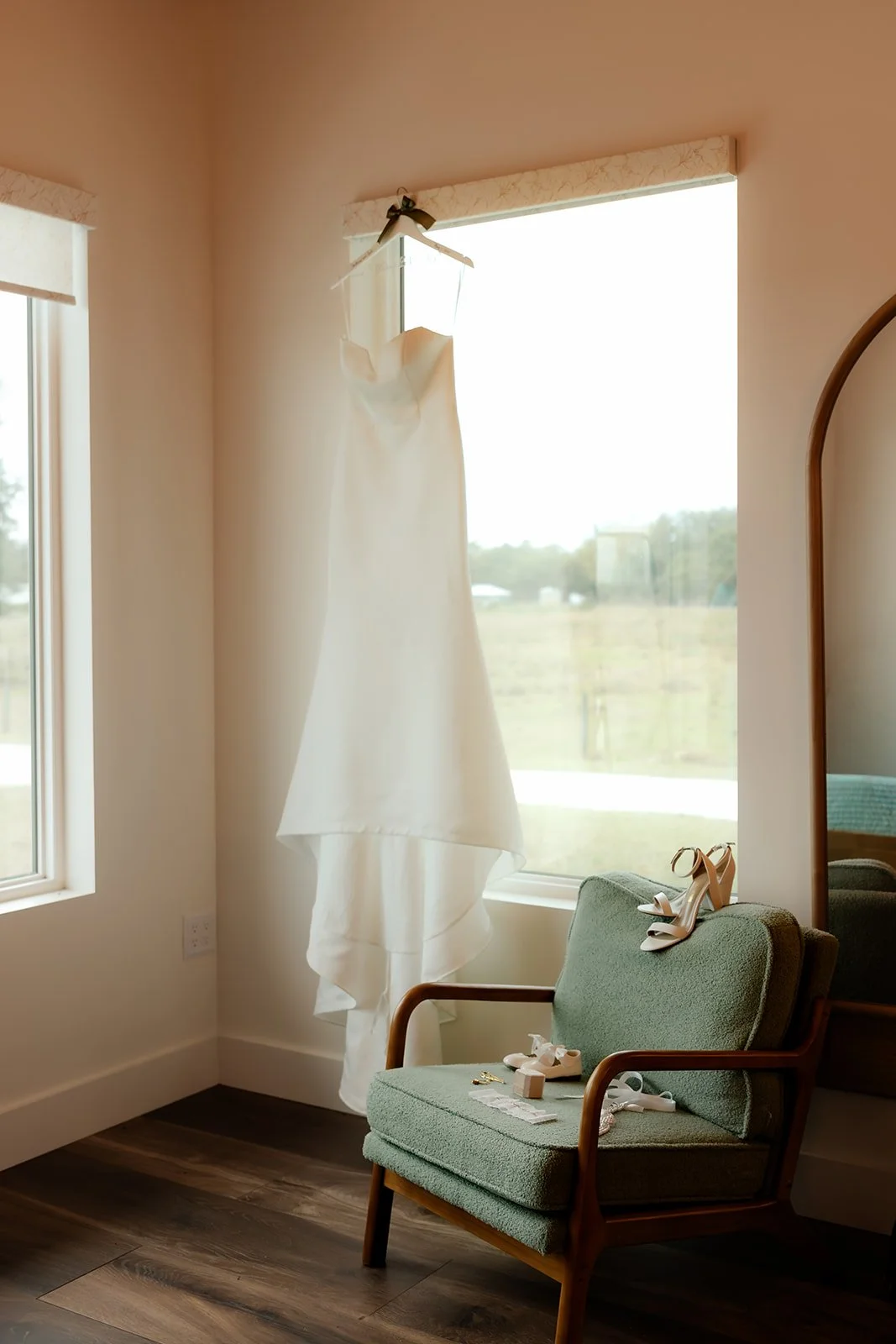 Bride's sweetheart wedding gown hanging in bridal suite window at Browns Grove Sarasota with green mid-century chair