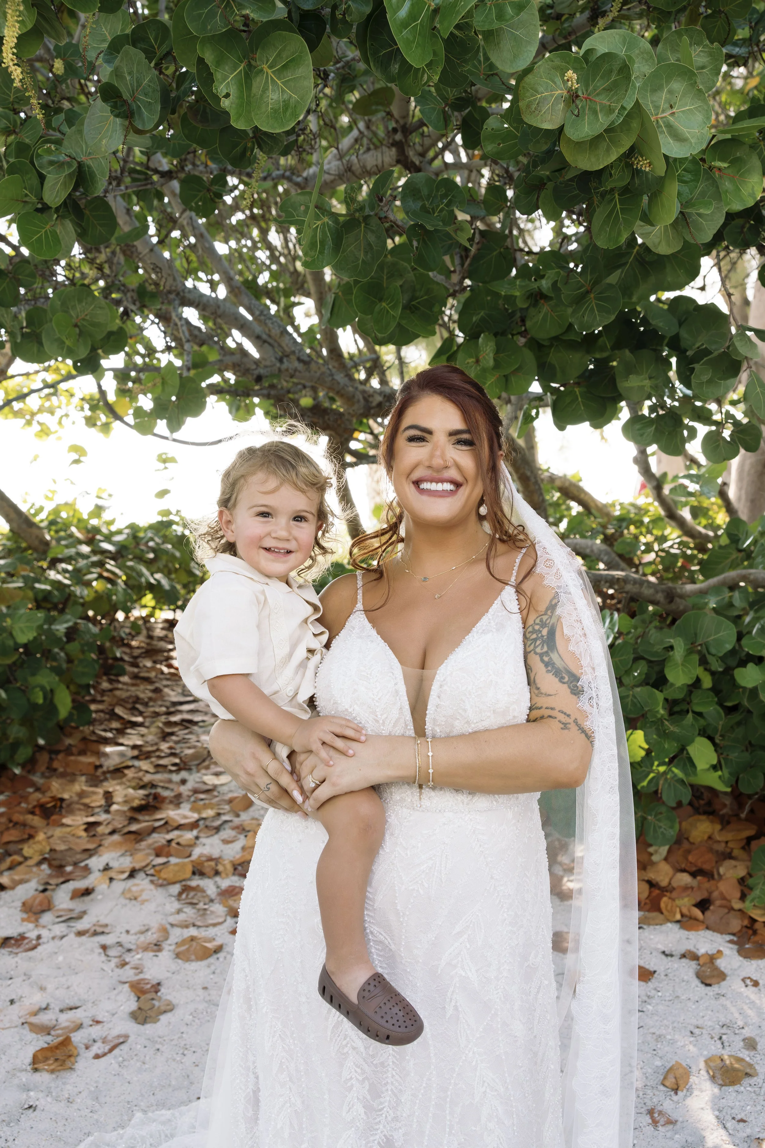bride-holding-child-candid-beach-moment-grand-pavilion-sandbar-anna-maria-island-wedding.jpg