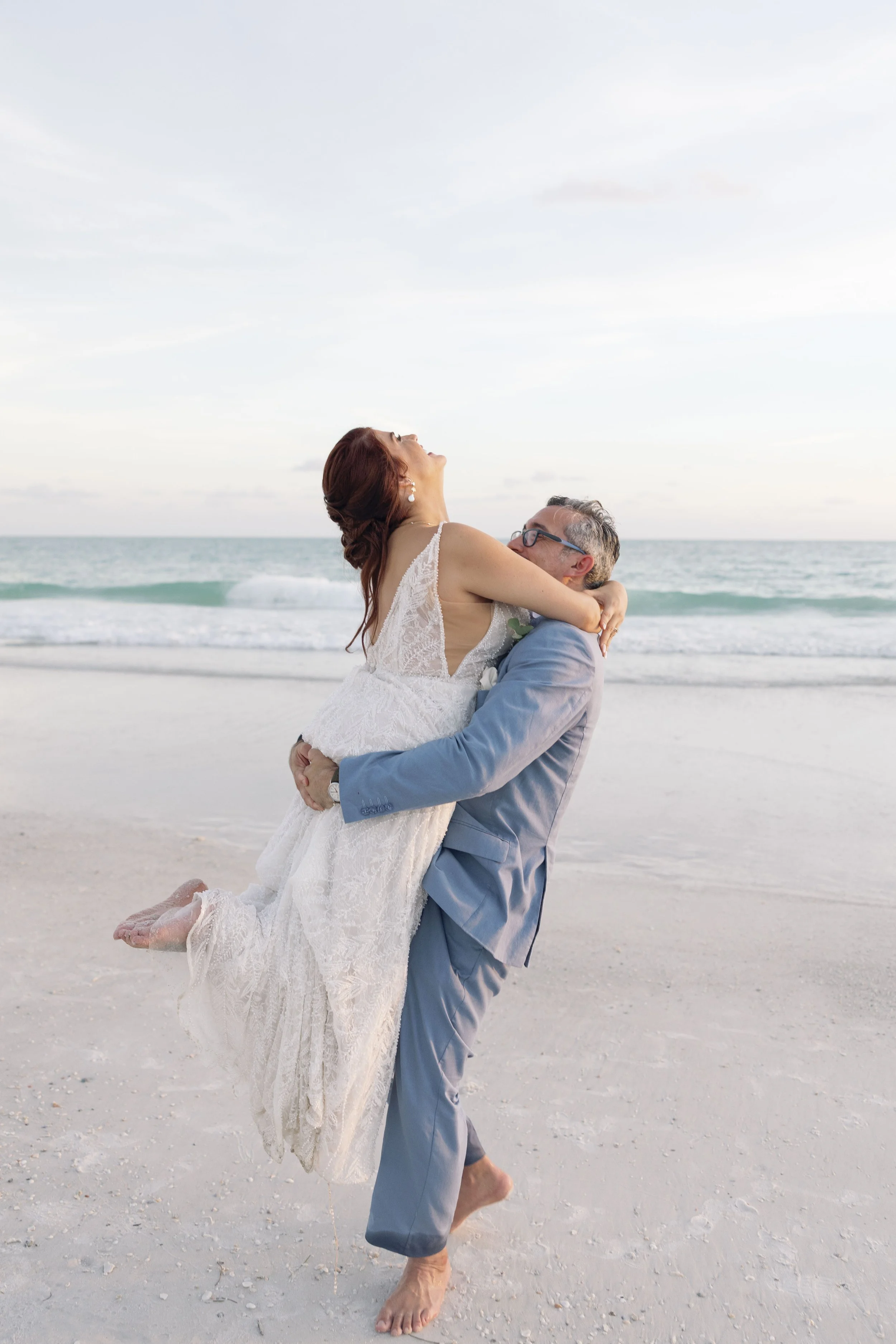 groom-lifting-bride-beach-veil-flowing-grand-pavilion-sandbar-anna-maria-island-wedding.jpg