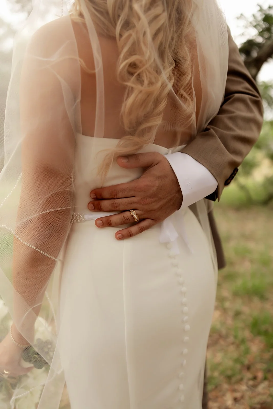 Detail shot of groom's hand with wedding ring resting on bride's waist, pearl-edged veil flowing around them — Browns Grove Sarasota