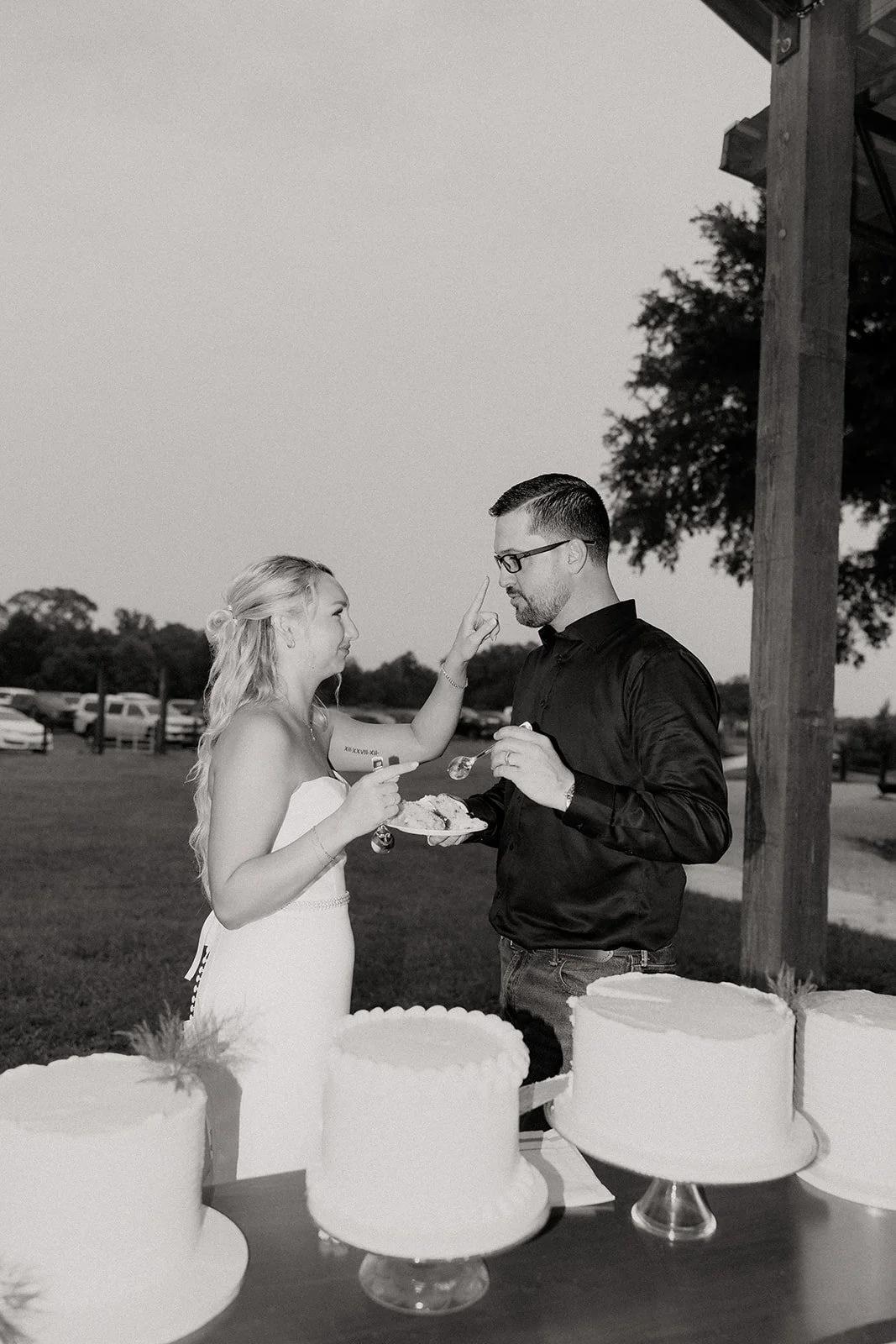 Black and white photo of bride putting cake on groom's nose playfully during cake cutting at Browns Grove Sarasota reception