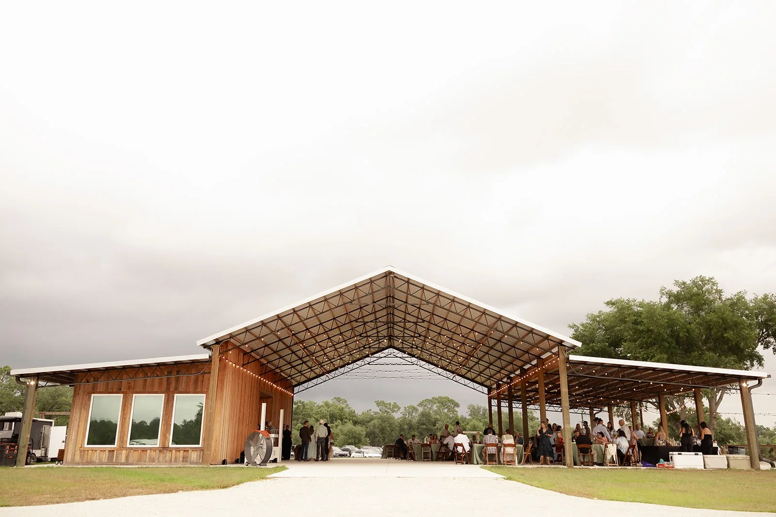 Wide shot of Browns Grove Sarasota open-air wedding pavilion with string lights and guests at reception under dramatic stormy sky