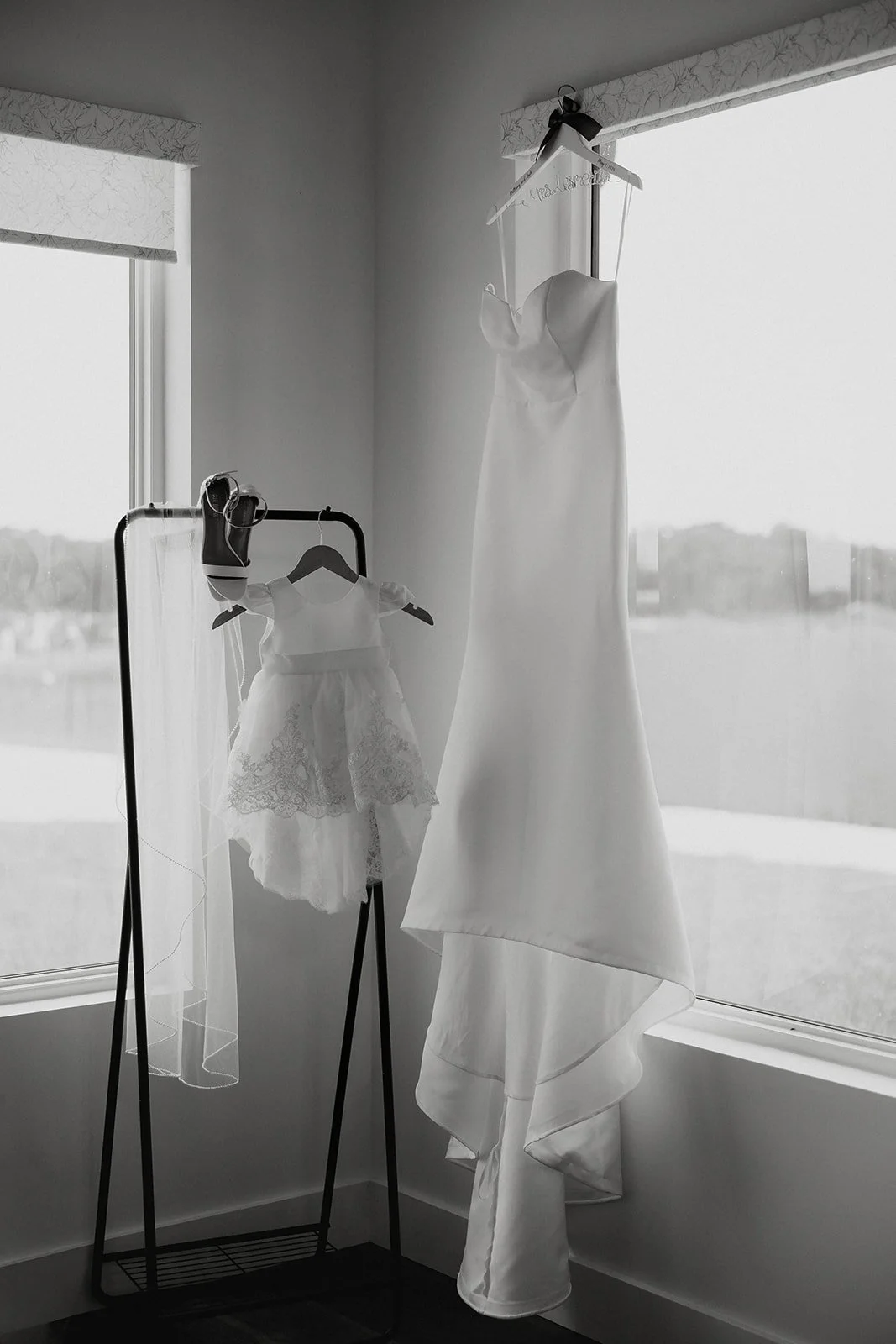 Wedding dress and matching flower girl dress hanging side by side on garment rack at Browns Grove Sarasota