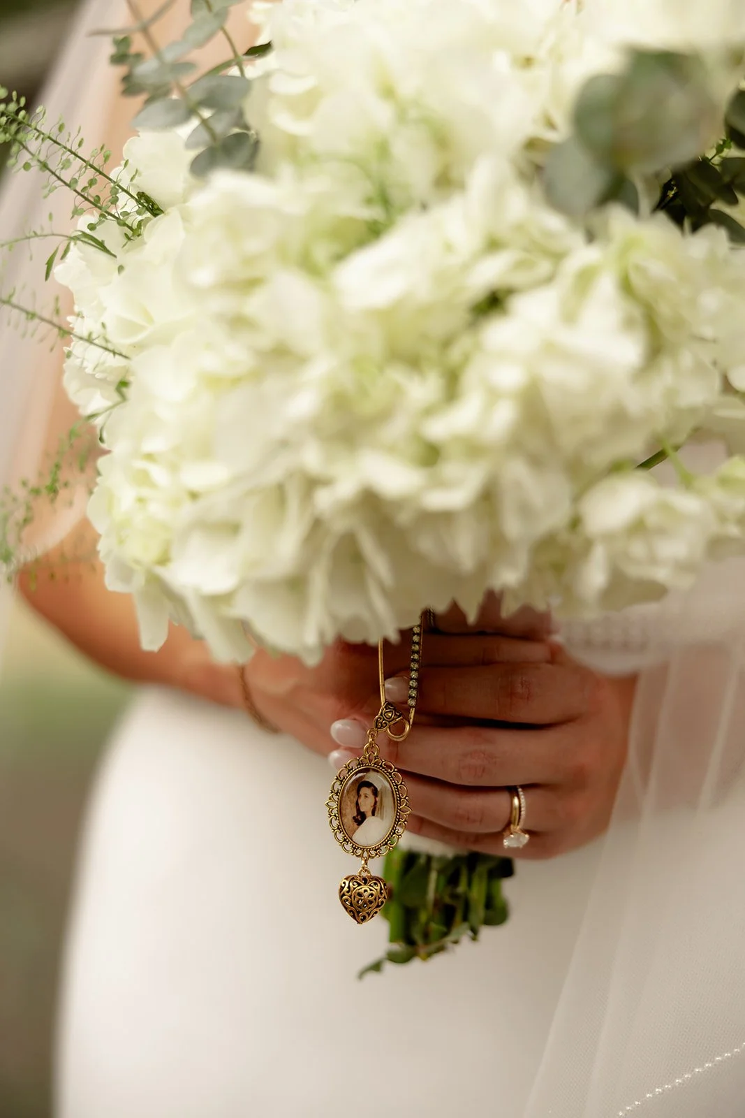 Close-up of white hydrangea and eucalyptus bridal bouquet with gold memorial locket charm pinned to the stems — Browns Grove Sarasota wedding