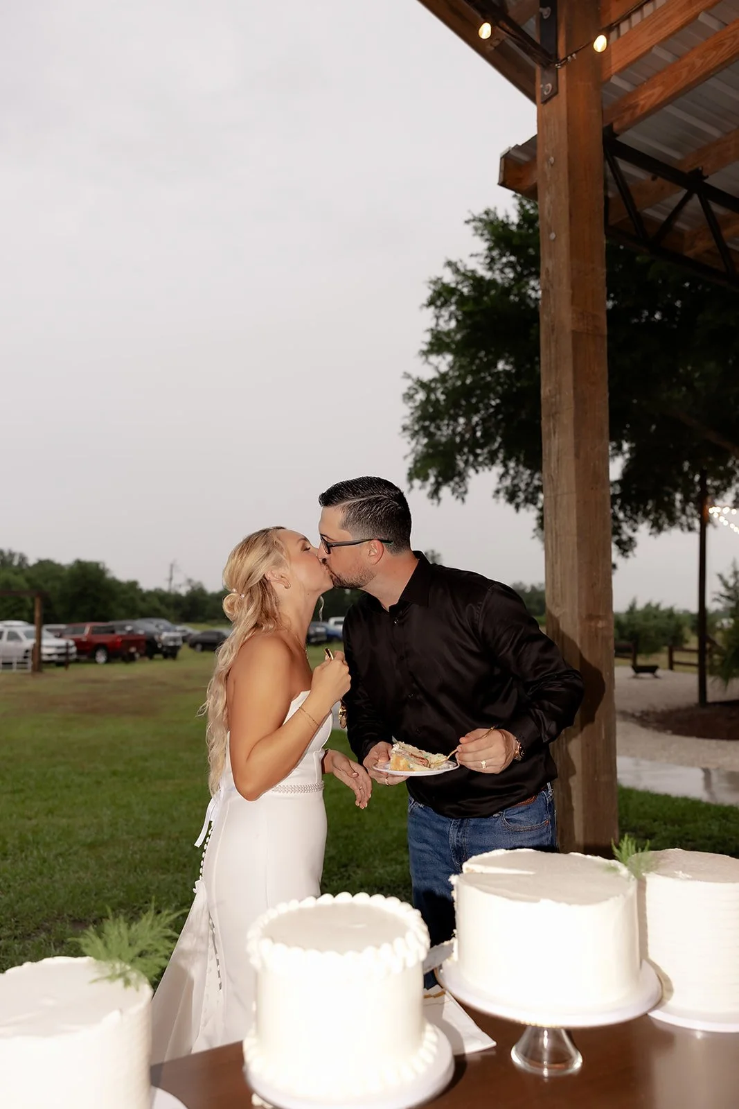 Bride and groom kissing at the cake table during reception at Browns Grove Sarasota with dramatic stormy sky behind them